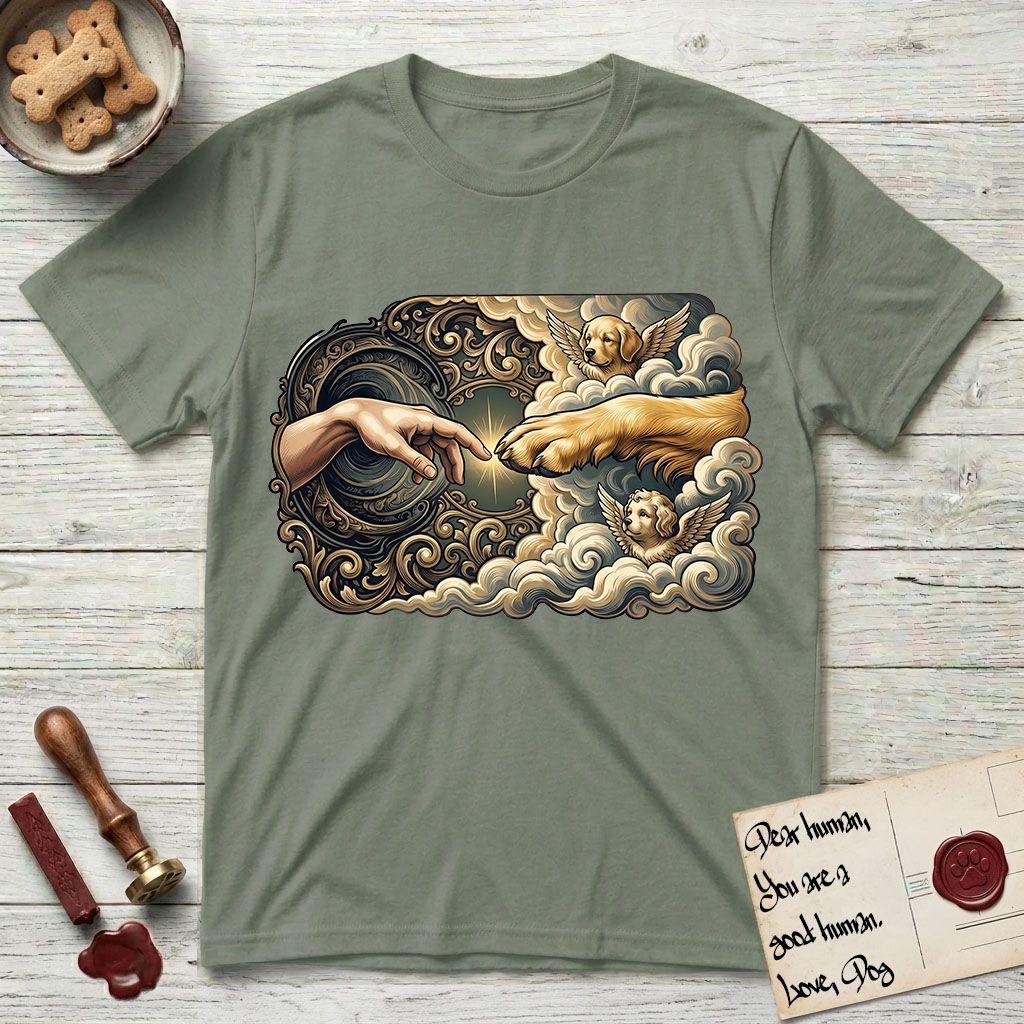 Creation of Adam T-Shirt flat lay in Sage, featuring a baroque ornamental frame with a Golden Retriever emerging from clouds extending a paw toward a reaching human hand, a small angel beside them, and a glowing point of contact.