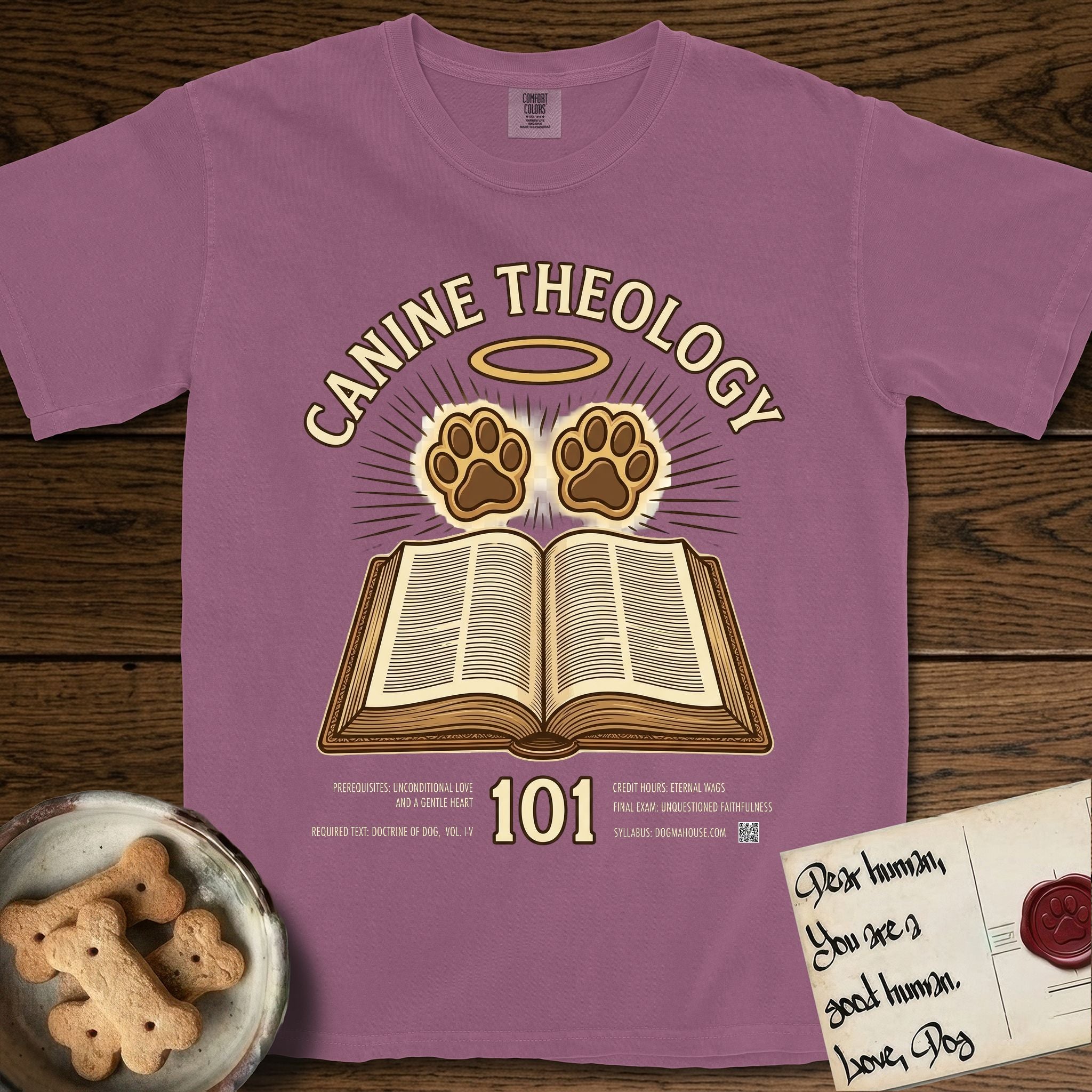 Canine Theology 101 T-Shirt flat lay in Berry, featuring a cream badge with an open book and two glowing paw prints rising above it, ringed by a circular halo.