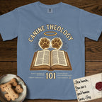 Canine Theology 101 T-Shirt flat lay in Blue Jean, featuring a cream badge with an open book and two glowing paw prints rising above it, ringed by a circular halo.
