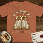 Canine Theology 101 T-Shirt flat lay in Yam, featuring a cream badge with an open book and two glowing paw prints rising above it, ringed by a circular halo.