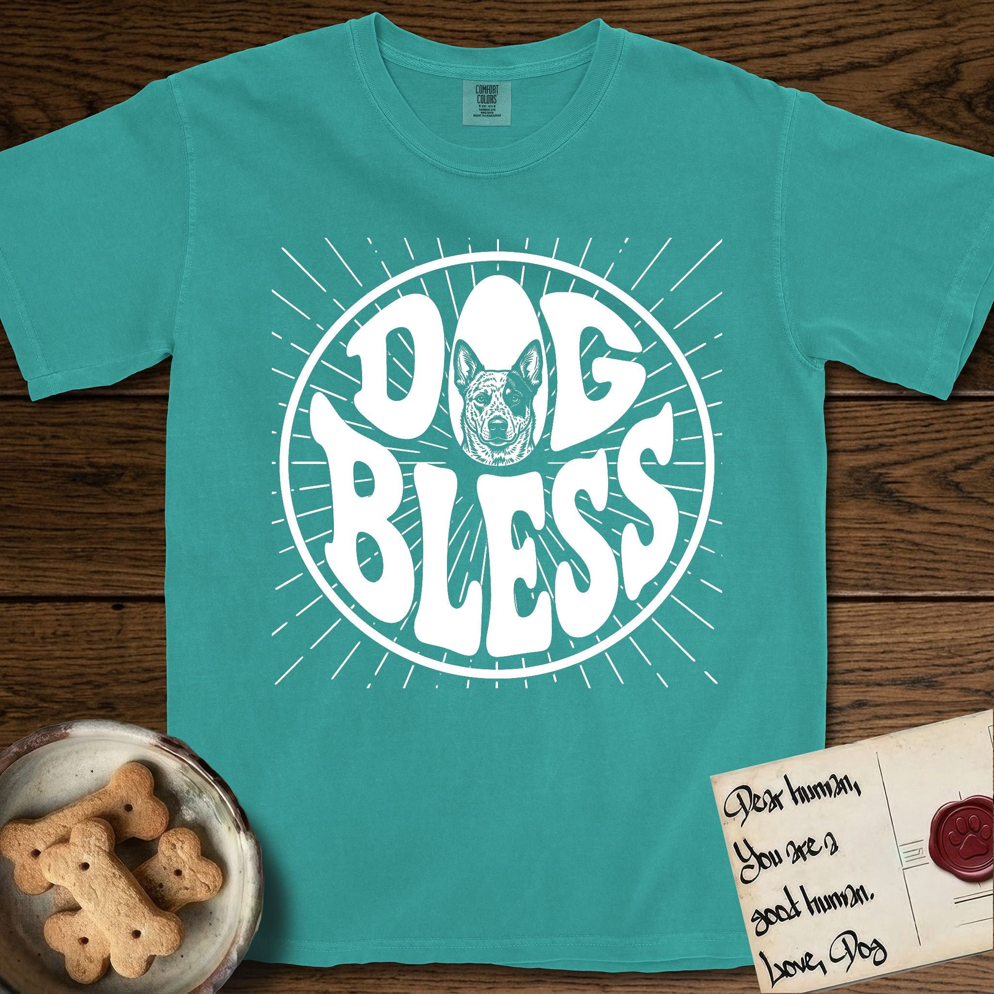 Dog Bless Australian Cattle Dog T-Shirt flat lay in Seafoam, featuring Retro bubble-letter badge reading DOG BLESS with a speckled Australian Cattle Dog face framed in the letter O, hand-drawn sunburst rays radiating outward.