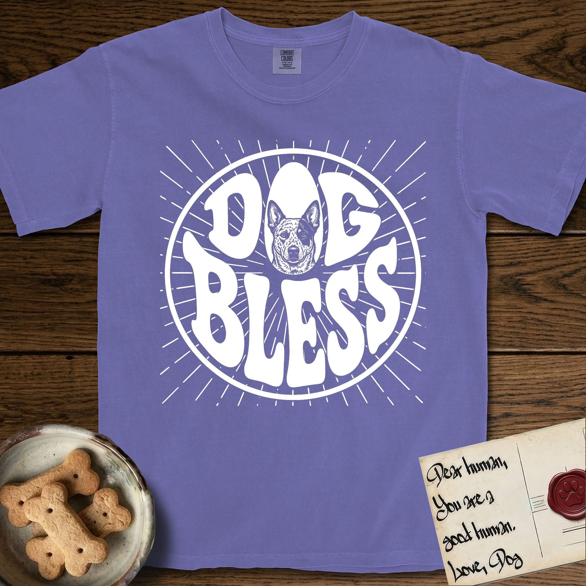 Dog Bless Australian Cattle Dog T-Shirt flat lay in Violet, featuring Retro bubble-letter badge reading DOG BLESS with a speckled Australian Cattle Dog face framed in the letter O, hand-drawn sunburst rays radiating outward.