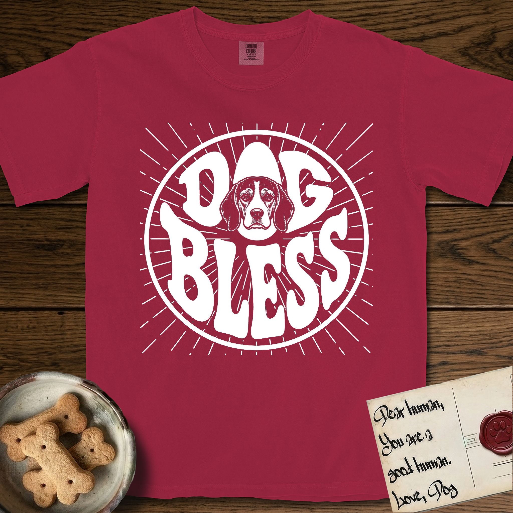 Dog Bless Beagle T-Shirt flat lay in Chili, featuring Retro bubble-letter badge reading DOG BLESS with a gentle Beagle face framed in the letter O, hand-drawn sunburst rays radiating outward.