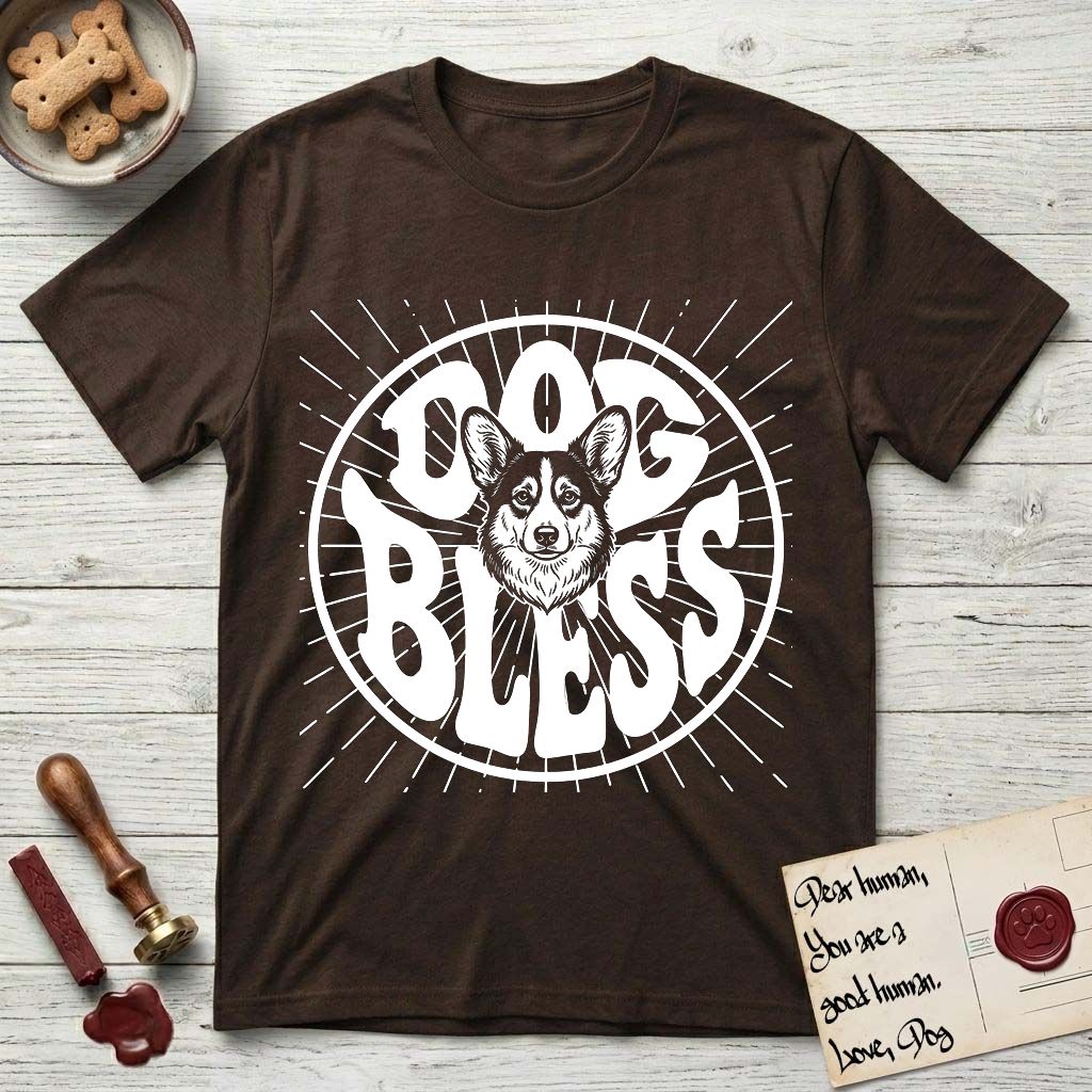 Dog Bless Corgi T-Shirt flat lay in Dark Chocolate, featuring Retro bubble-letter badge reading DOG BLESS with a smiling Corgi face framed in the letter O, chest fluff spilling below the letter, hand-drawn sunburst rays radiating outward.