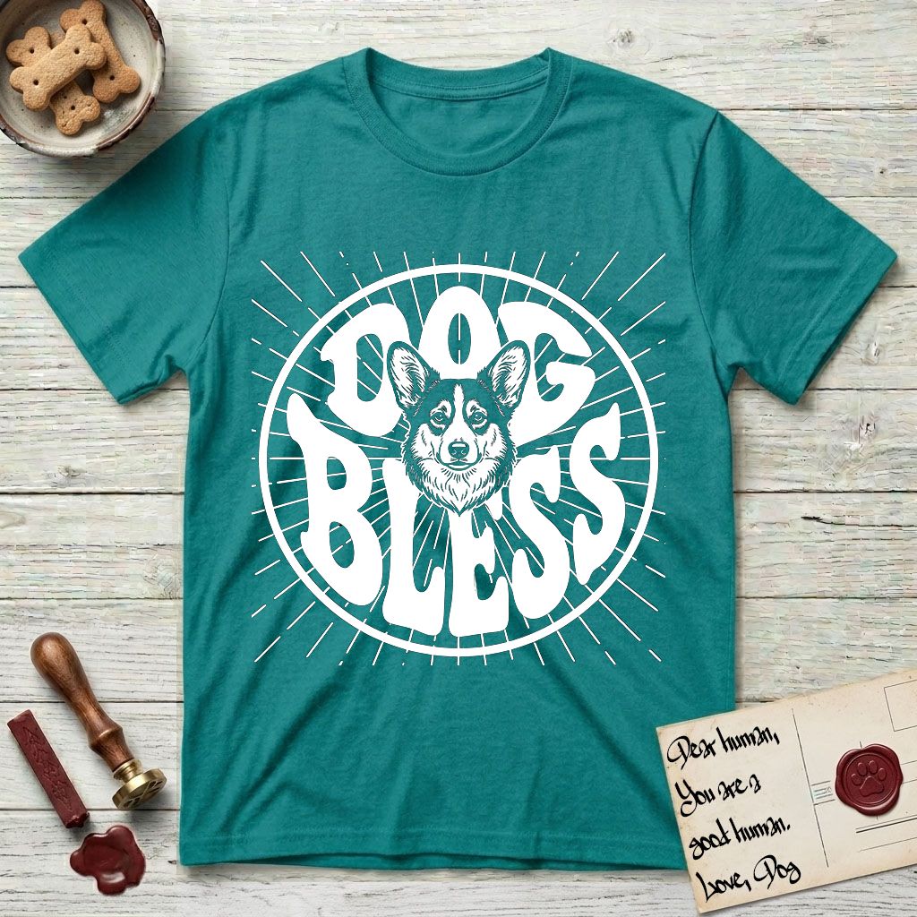 Dog Bless Corgi T-Shirt flat lay in Jade Dome, featuring Retro bubble-letter badge reading DOG BLESS with a smiling Corgi face framed in the letter O, chest fluff spilling below the letter, hand-drawn sunburst rays radiating outward.