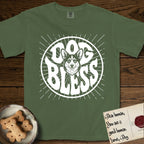 Dog Bless Corgi T-Shirt flat lay in Moss, featuring Retro bubble-letter badge reading DOG BLESS with a smiling Corgi face framed in the letter O, chest fluff spilling below the letter, hand-drawn sunburst rays radiating outward.