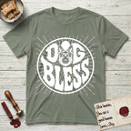 Dog Bless German Shepherd T-Shirt flat lay in Sage, featuring Retro bubble-letter badge reading DOG BLESS with a German Shepherd face with tall upright ears framed in the letter O, hand-drawn sunburst rays radiating outward.