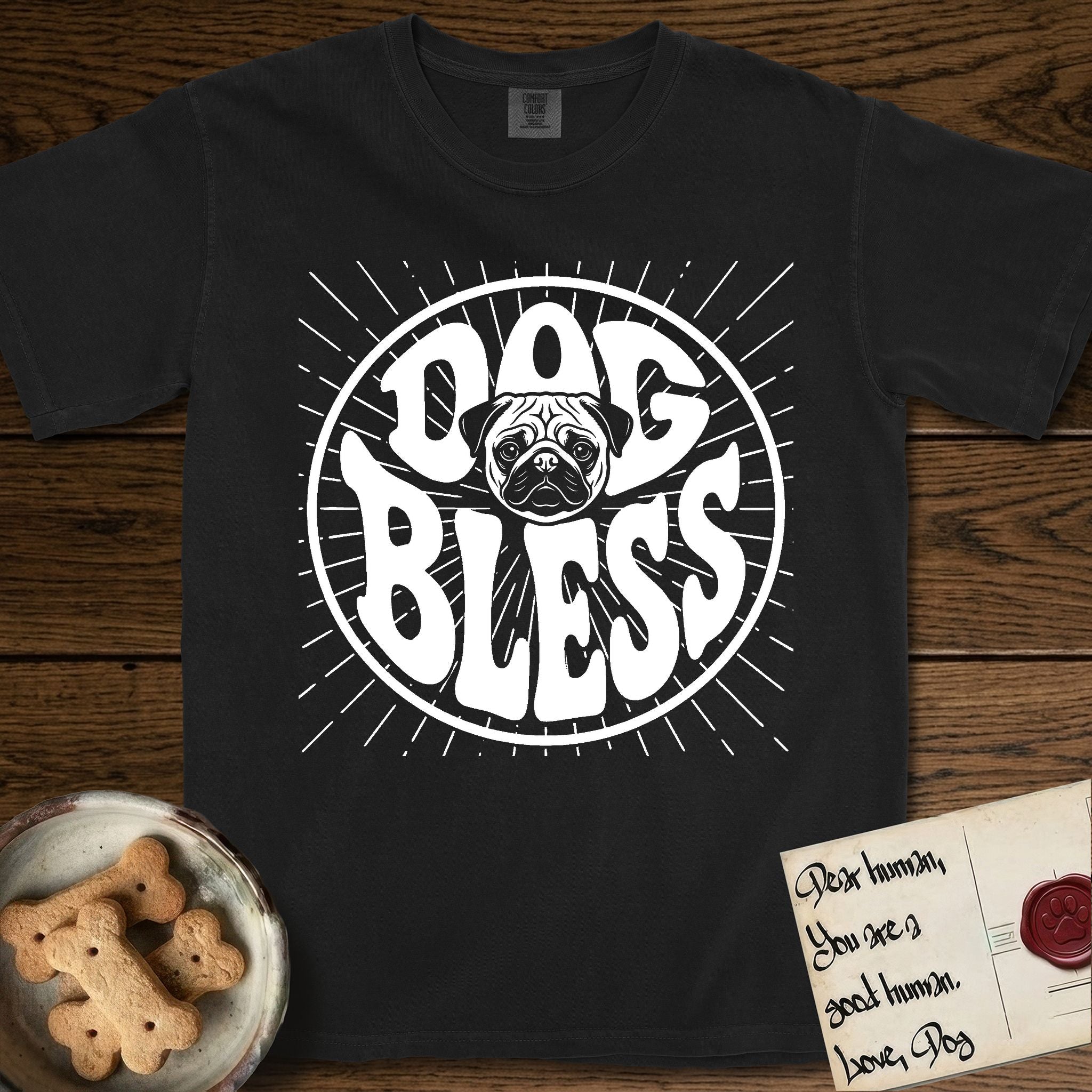 Dog Bless Pug T-Shirt flat lay in Black, featuring Retro bubble-letter badge reading DOG BLESS with a wrinkled Pug face with large round eyes framed in the letter O, hand-drawn sunburst rays radiating outward.