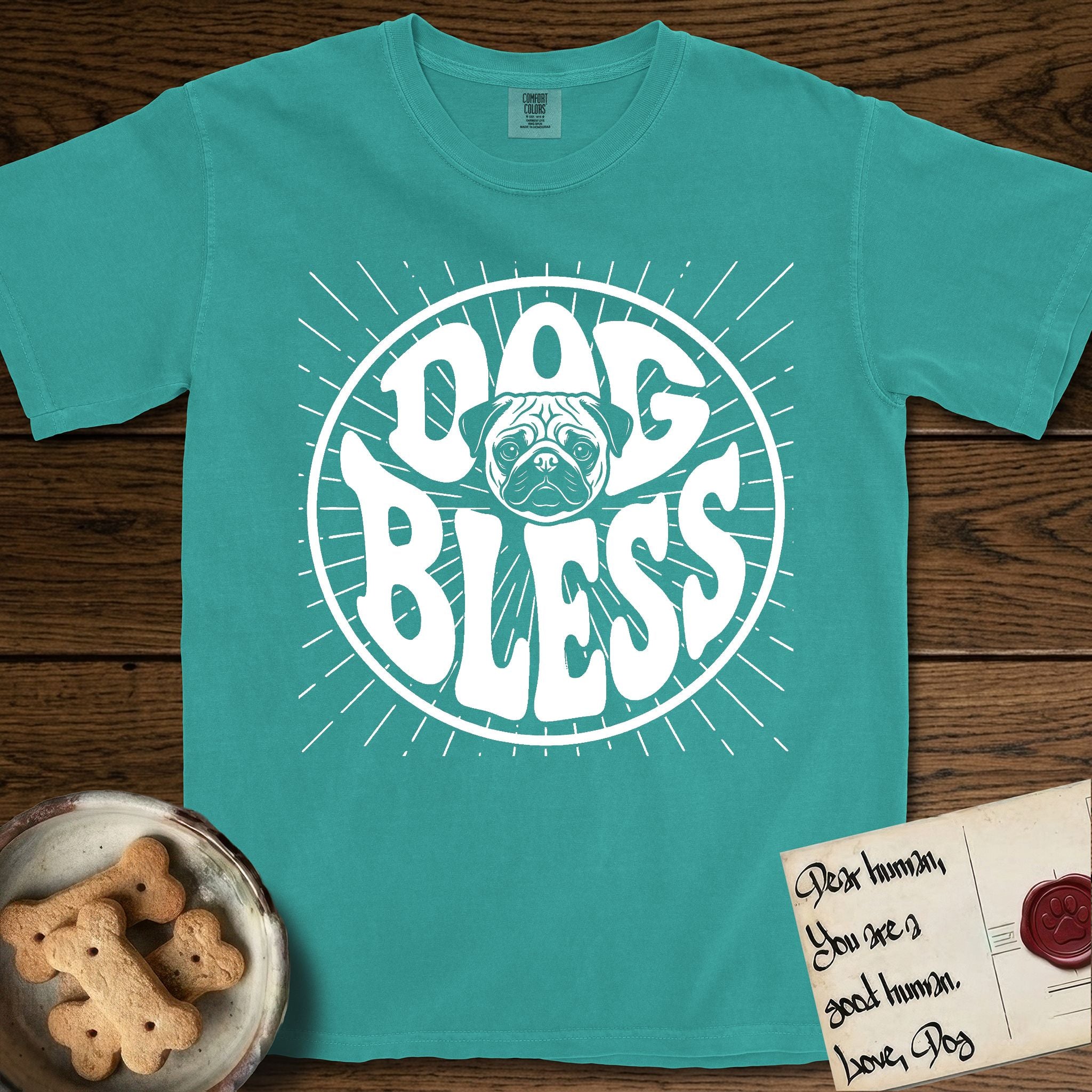 Dog Bless Pug T-Shirt flat lay in Seafoam, featuring Retro bubble-letter badge reading DOG BLESS with a wrinkled Pug face with large round eyes framed in the letter O, hand-drawn sunburst rays radiating outward.
