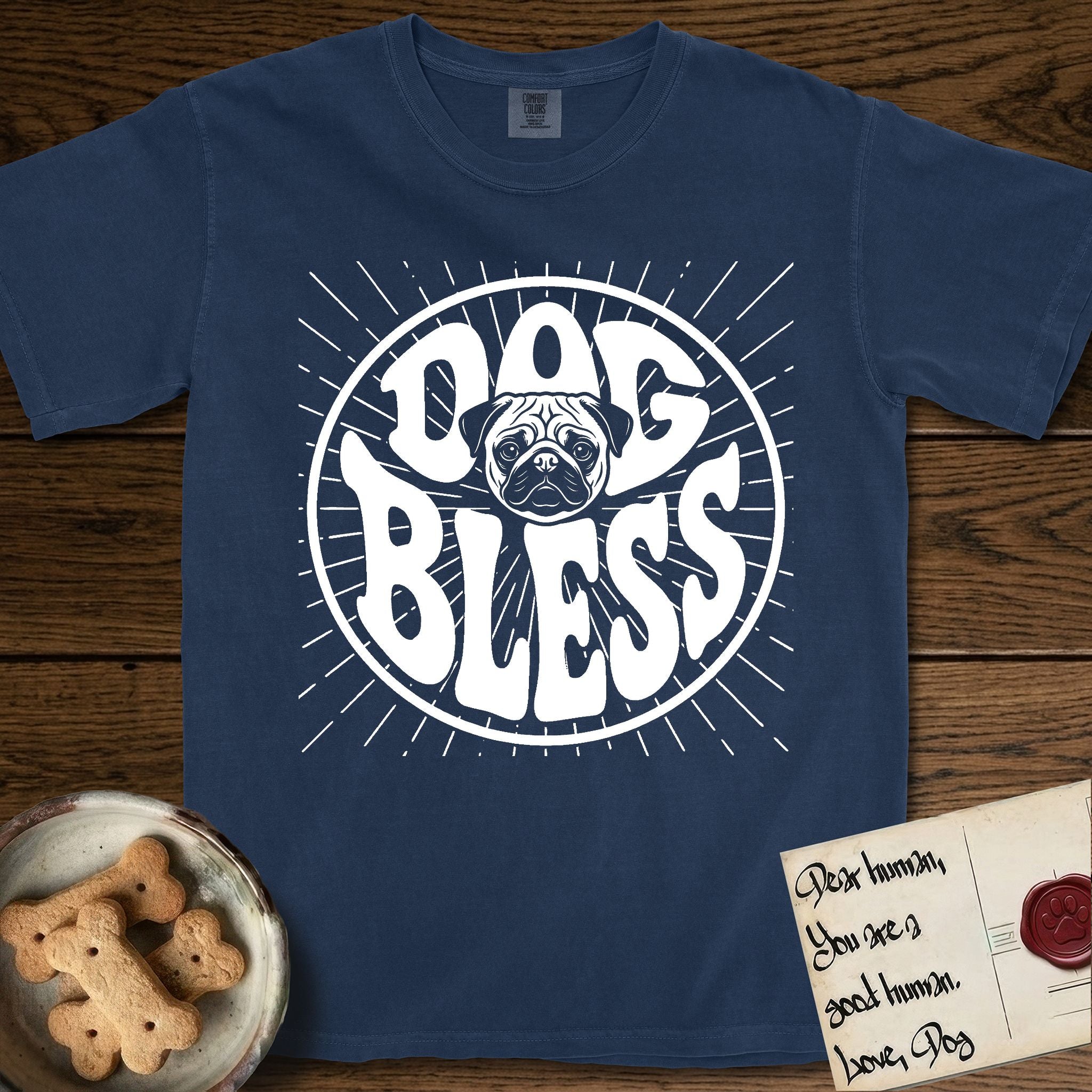 Dog Bless Pug T-Shirt flat lay in True Navy, featuring Retro bubble-letter badge reading DOG BLESS with a wrinkled Pug face with large round eyes framed in the letter O, hand-drawn sunburst rays radiating outward.
