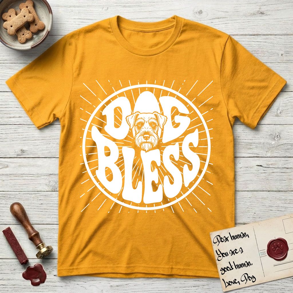 Dog Bless Schnauzer T-Shirt flat lay in Gold, featuring Retro bubble-letter badge reading DOG BLESS with a bearded Schnauzer face with bushy eyebrows framed in the letter O, hand-drawn sunburst rays radiating outward.