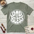 Dog Bless Schnauzer T-Shirt flat lay in Sage, featuring Retro bubble-letter badge reading DOG BLESS with a bearded Schnauzer face with bushy eyebrows framed in the letter O, hand-drawn sunburst rays radiating outward.