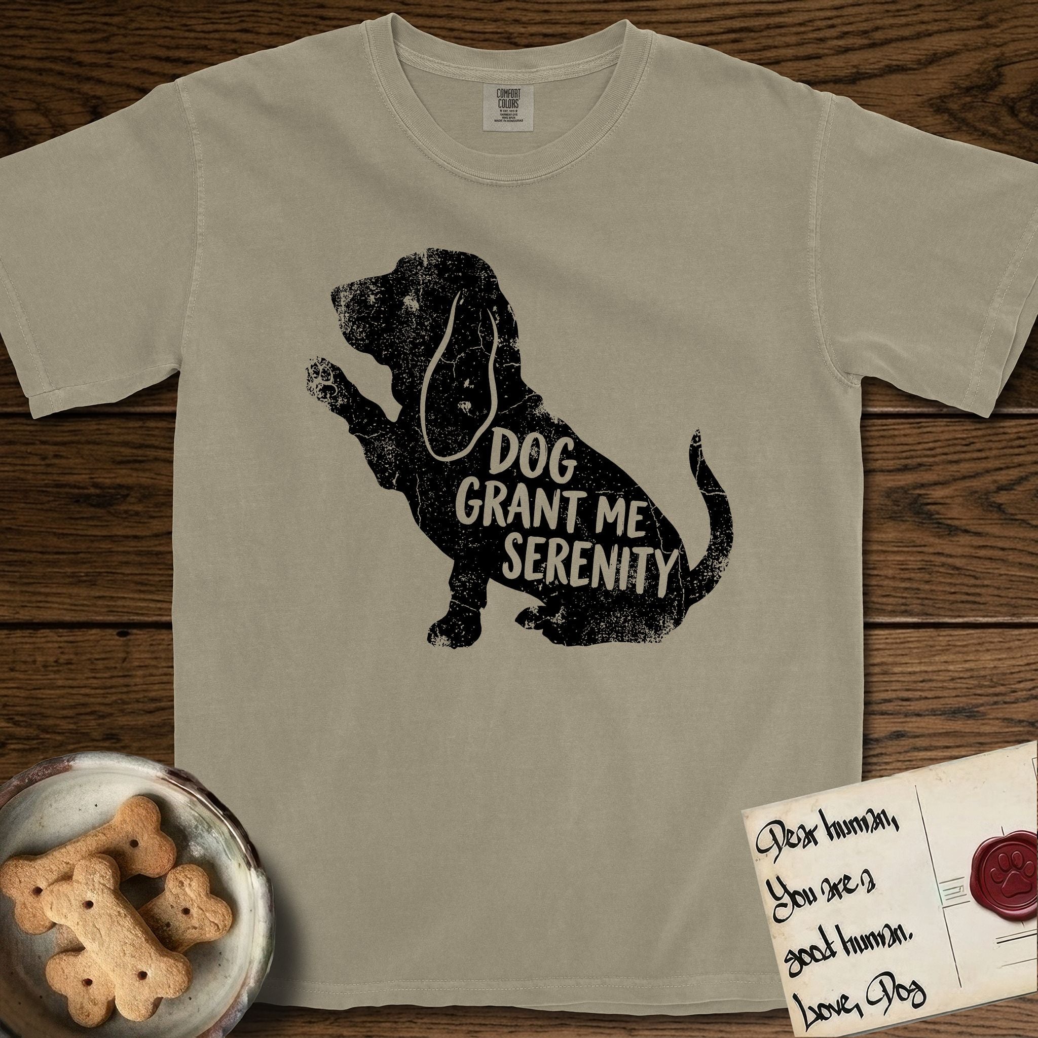 Serenity Basset Hound T-Shirt flat lay in Khaki, featuring Distressed black screen print silhouette of a Basset Hound sitting in profile with one paw raised and long ears hanging, the words DOG GRANT ME SERENITY showing through his body in the shirt color.