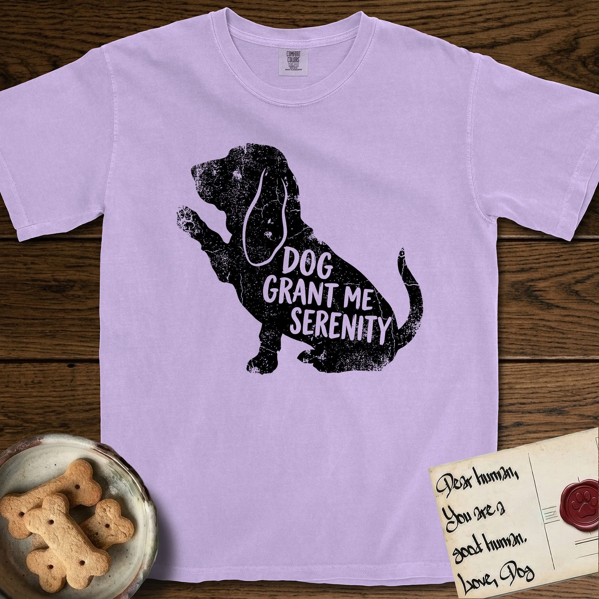 Serenity Basset Hound T-Shirt flat lay in Orchid, featuring Distressed black screen print silhouette of a Basset Hound sitting in profile with one paw raised and long ears hanging, the words DOG GRANT ME SERENITY showing through his body in the shirt color.