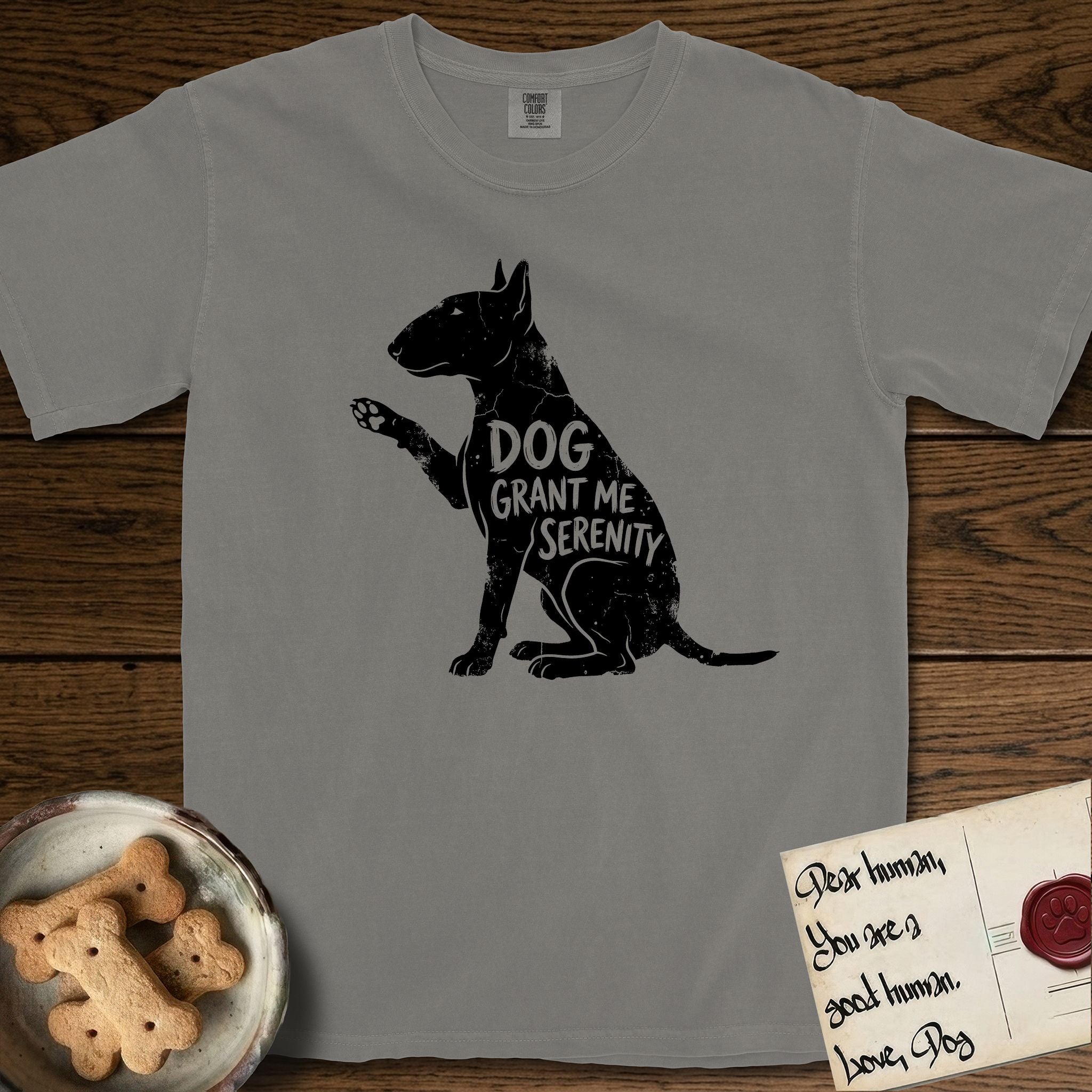 Serenity Bull Terrier T-Shirt flat lay in Grey, featuring Distressed black screen print silhouette of a Bull Terrier sitting in profile with one paw raised and an egg-shaped head, the words DOG GRANT ME SERENITY showing through her body in the shirt color.