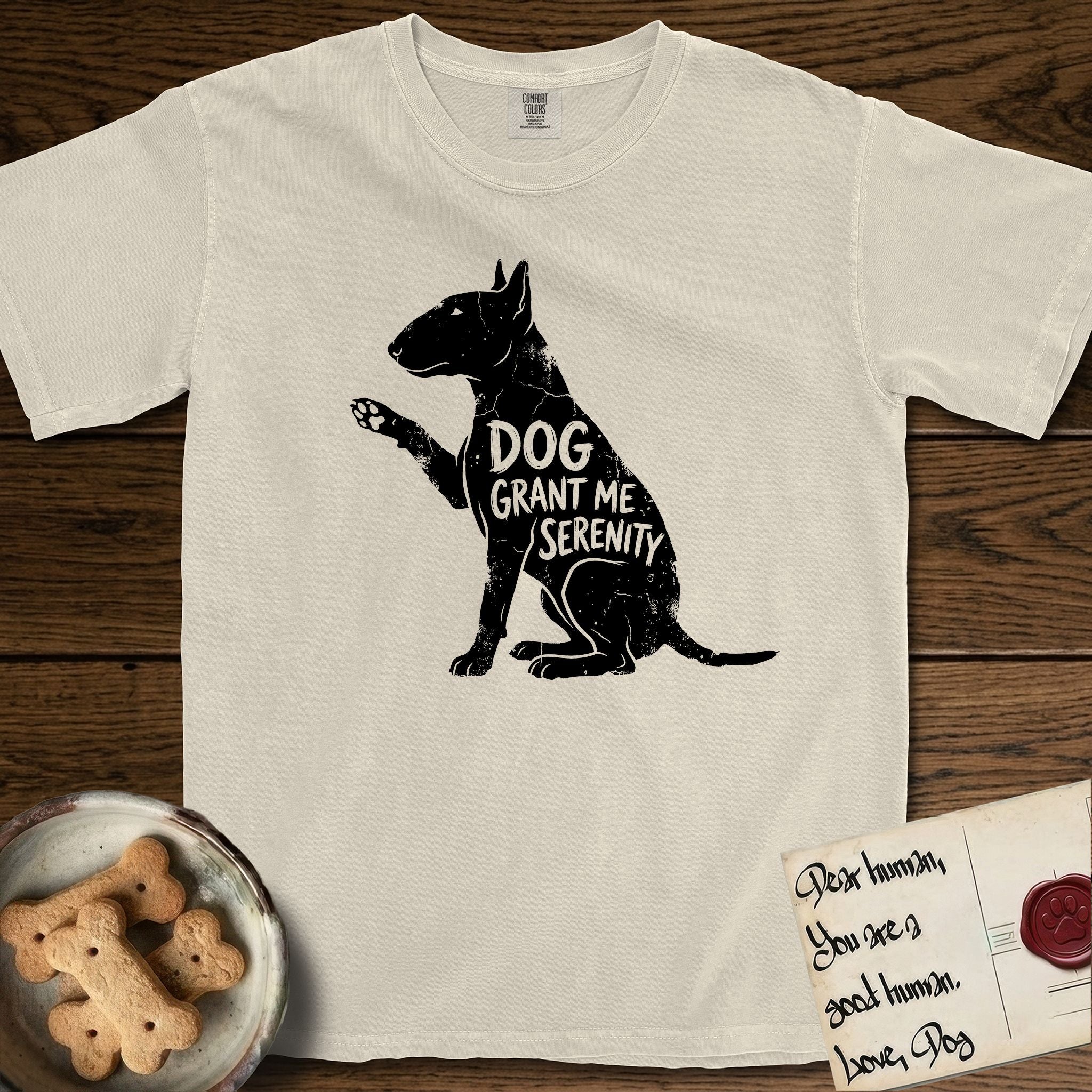 Serenity Bull Terrier T-Shirt flat lay in Ivory, featuring Distressed black screen print silhouette of a Bull Terrier sitting in profile with one paw raised and an egg-shaped head, the words DOG GRANT ME SERENITY showing through her body in the shirt color.