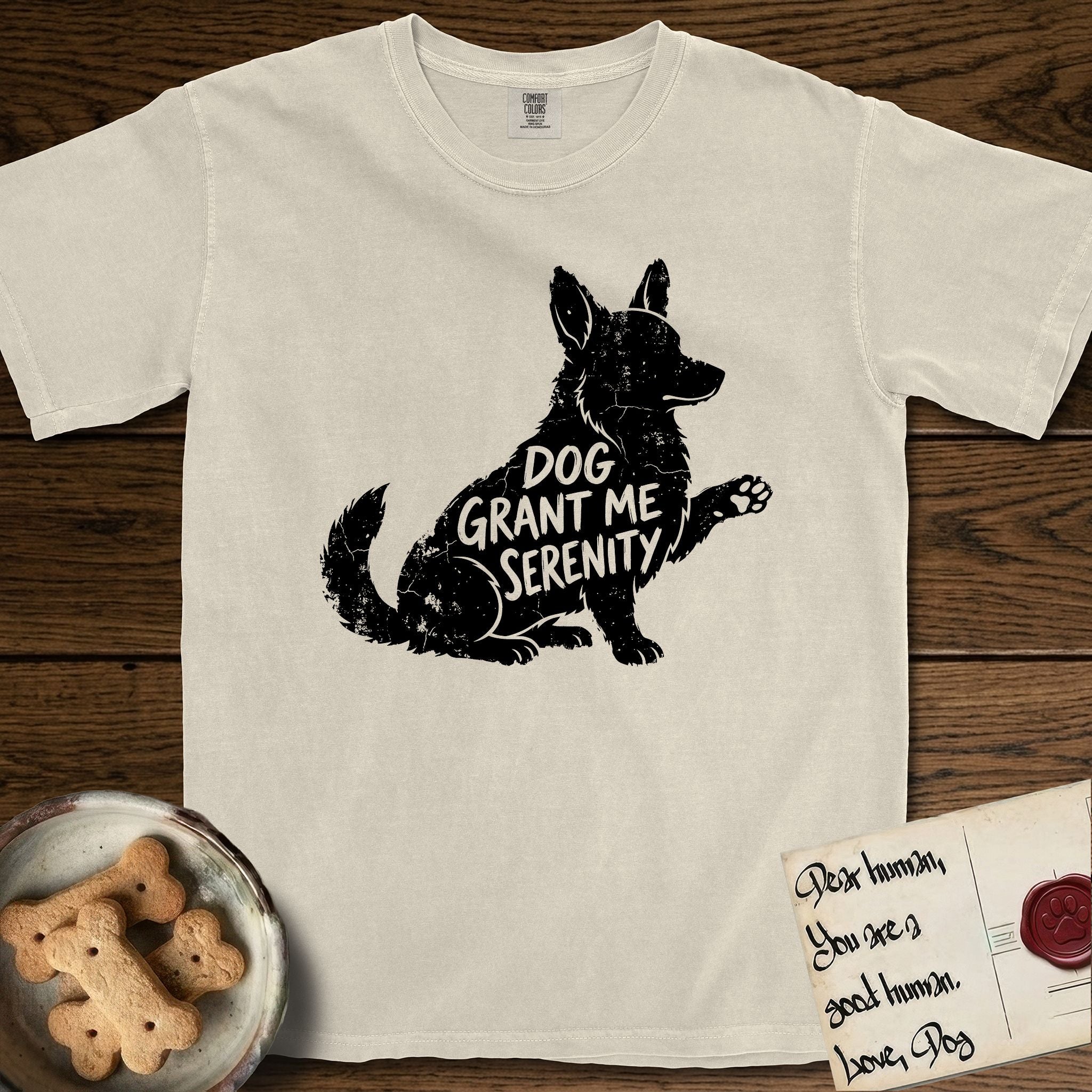 Serenity Corgi T-Shirt flat lay in Ivory, featuring Distressed black screen print silhouette of a Corgi sitting in profile with one paw raised, upright ears and a full brush tail, the words DOG GRANT ME SERENITY showing through his body in the shirt color.