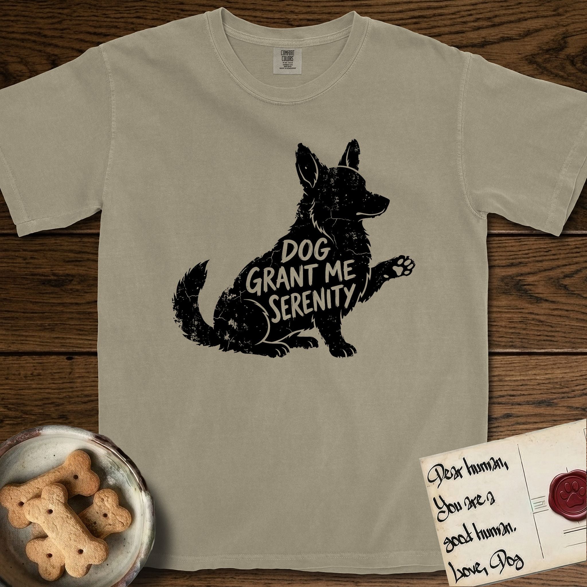 Serenity Corgi T-Shirt flat lay in Khaki, featuring Distressed black screen print silhouette of a Corgi sitting in profile with one paw raised, upright ears and a full brush tail, the words DOG GRANT ME SERENITY showing through his body in the shirt color.