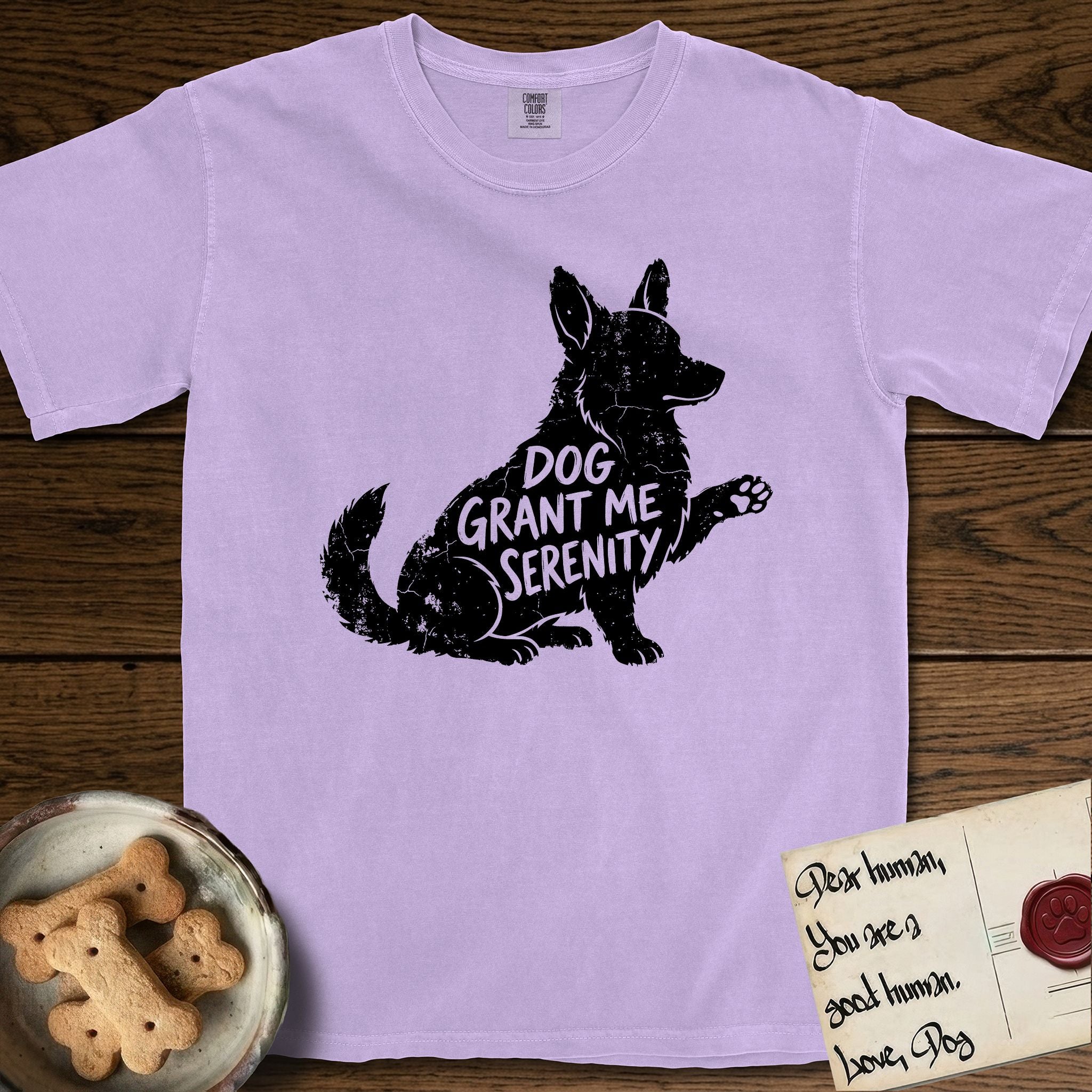 Serenity Corgi T-Shirt flat lay in Orchid, featuring Distressed black screen print silhouette of a Corgi sitting in profile with one paw raised, upright ears and a full brush tail, the words DOG GRANT ME SERENITY showing through his body in the shirt color.