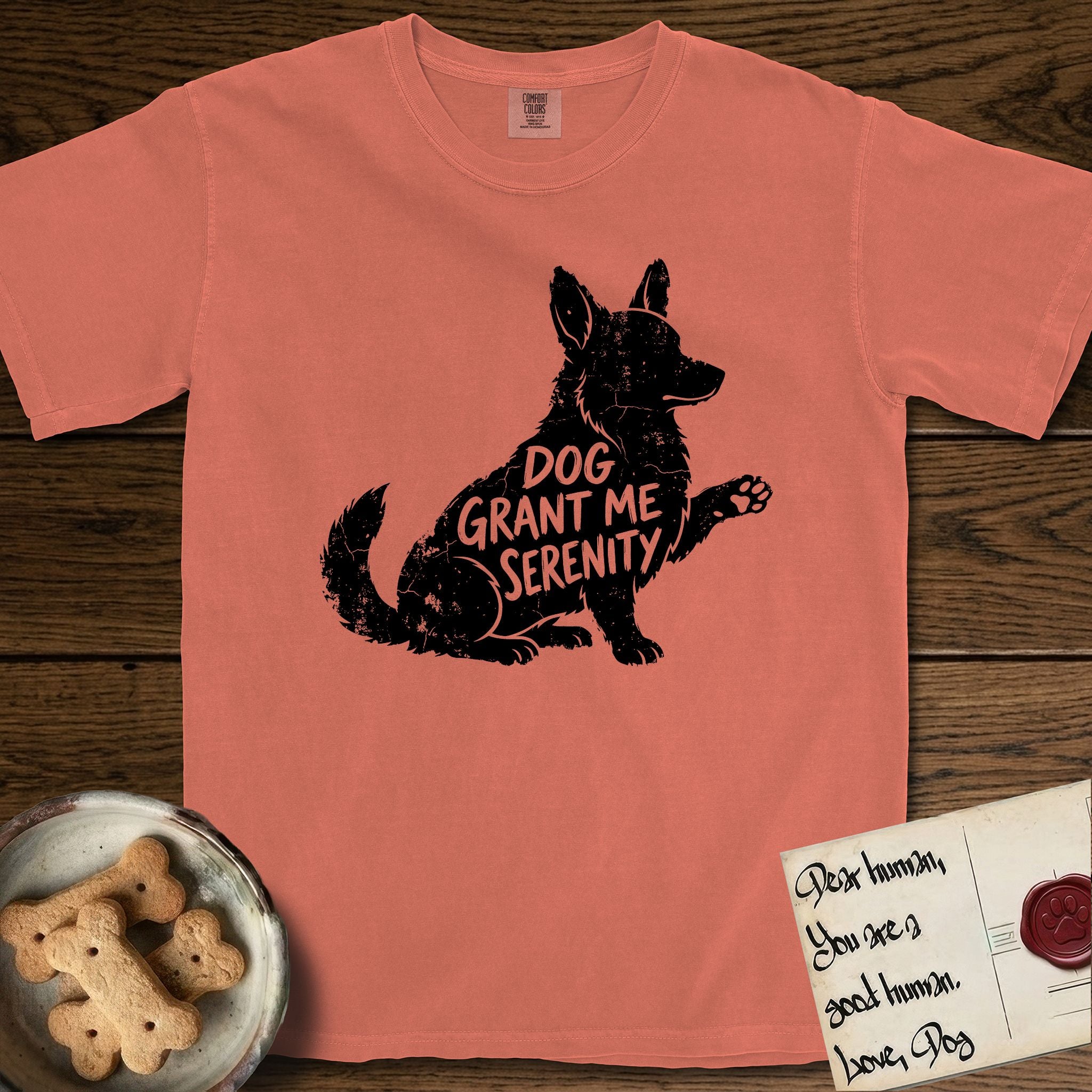 Serenity Corgi T-Shirt flat lay in Terracotta, featuring Distressed black screen print silhouette of a Corgi sitting in profile with one paw raised, upright ears and a full brush tail, the words DOG GRANT ME SERENITY showing through his body in the shirt color.