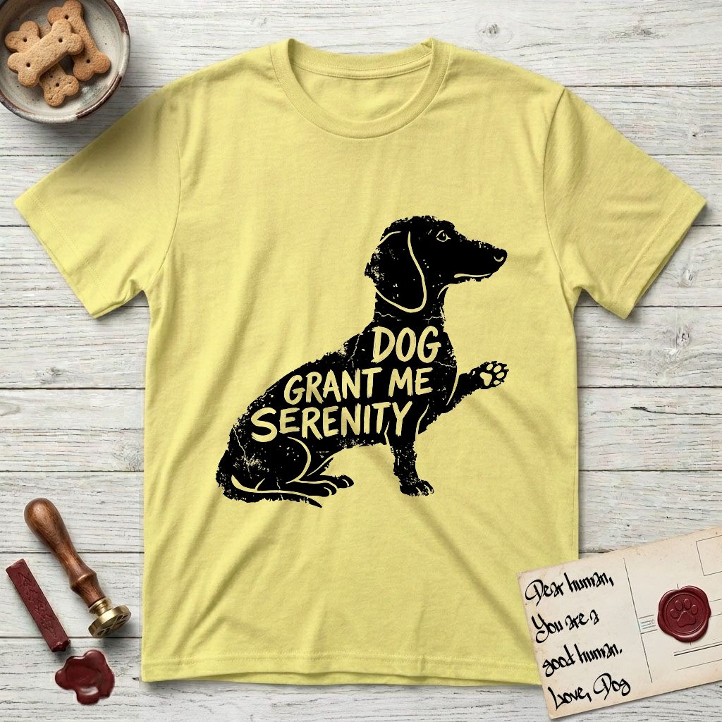 Serenity Dachshund T-Shirt flat lay in Cornsilk, featuring Distressed black screen print silhouette of a Dachshund sitting in profile with one paw raised, a long low body and long hanging ears, the words DOG GRANT ME SERENITY showing through her body in the shirt color.
