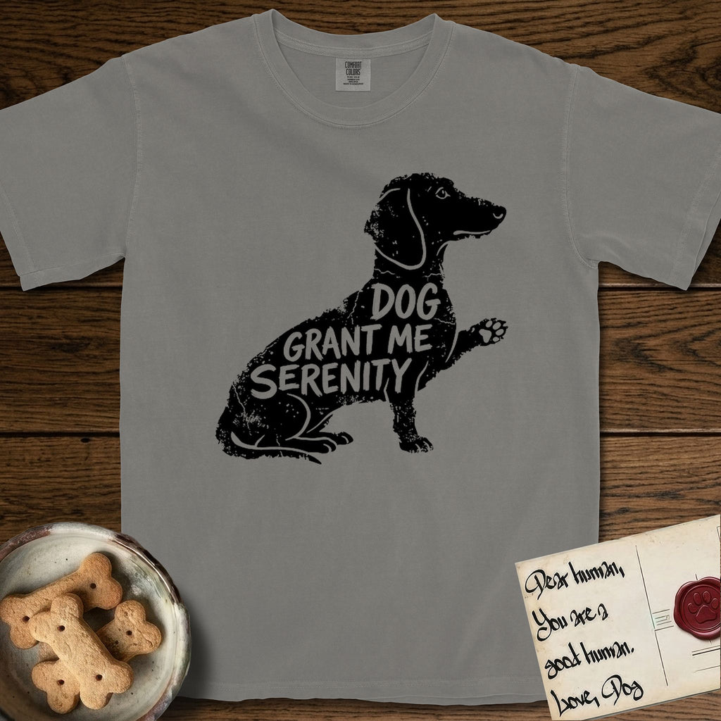 Serenity Dachshund T-Shirt flat lay in Grey, featuring Distressed black screen print silhouette of a Dachshund sitting in profile with one paw raised, a long low body and long hanging ears, the words DOG GRANT ME SERENITY showing through her body in the shirt color.