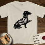 Serenity Dachshund T-Shirt flat lay in Ivory, featuring Distressed black screen print silhouette of a Dachshund sitting in profile with one paw raised, a long low body and long hanging ears, the words DOG GRANT ME SERENITY showing through her body in the shirt color.