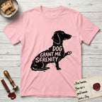 Serenity Dachshund T-Shirt flat lay in Light Pink, featuring Distressed black screen print silhouette of a Dachshund sitting in profile with one paw raised, a long low body and long hanging ears, the words DOG GRANT ME SERENITY showing through her body in the shirt color.