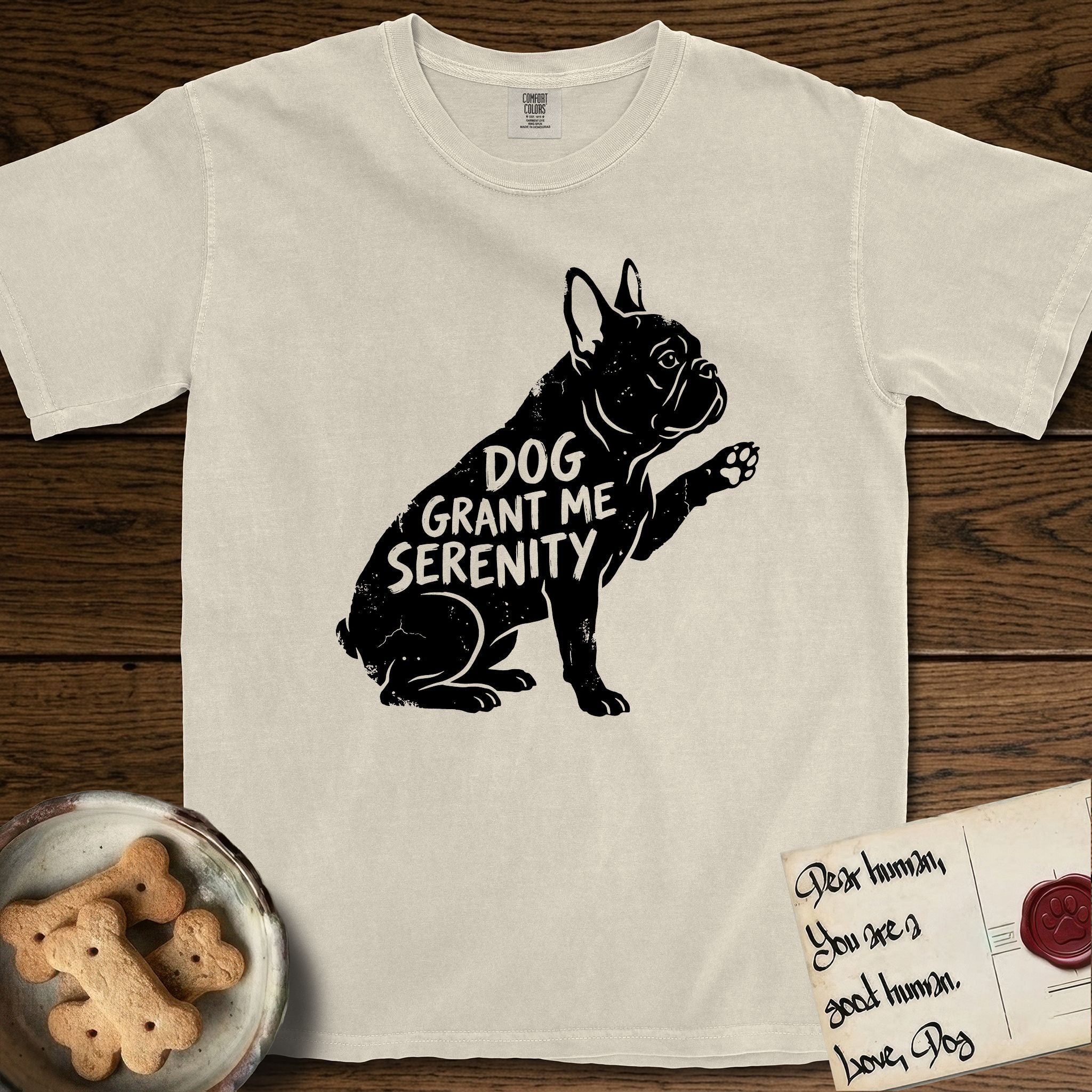Serenity French Bulldog T-Shirt flat lay in Ivory, featuring Distressed black screen print silhouette of a French Bulldog sitting in profile with one paw raised and large upright bat ears, the words DOG GRANT ME SERENITY showing through his body in the shirt color.