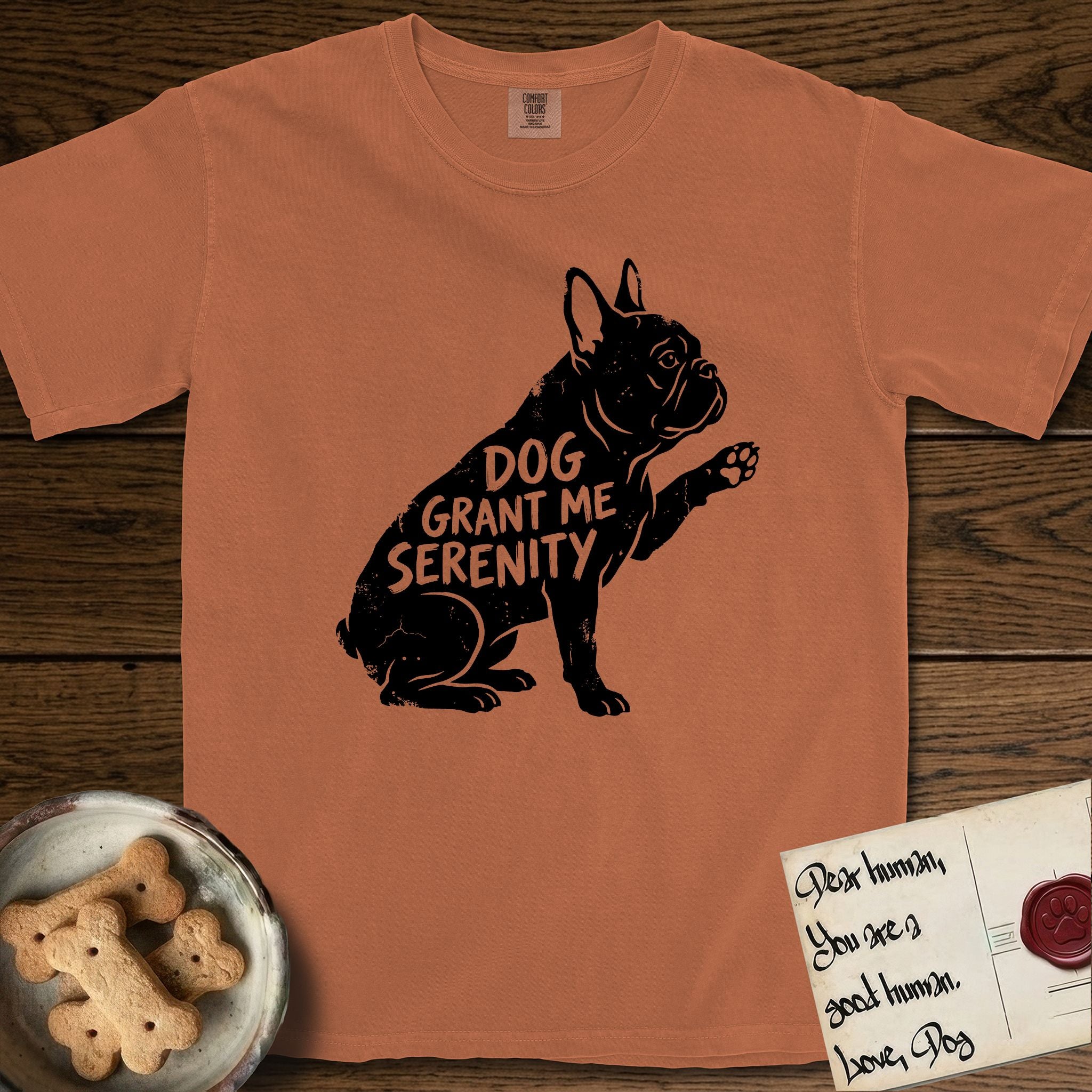Serenity French Bulldog T-Shirt flat lay in Yam, featuring Distressed black screen print silhouette of a French Bulldog sitting in profile with one paw raised and large upright bat ears, the words DOG GRANT ME SERENITY showing through his body in the shirt color.