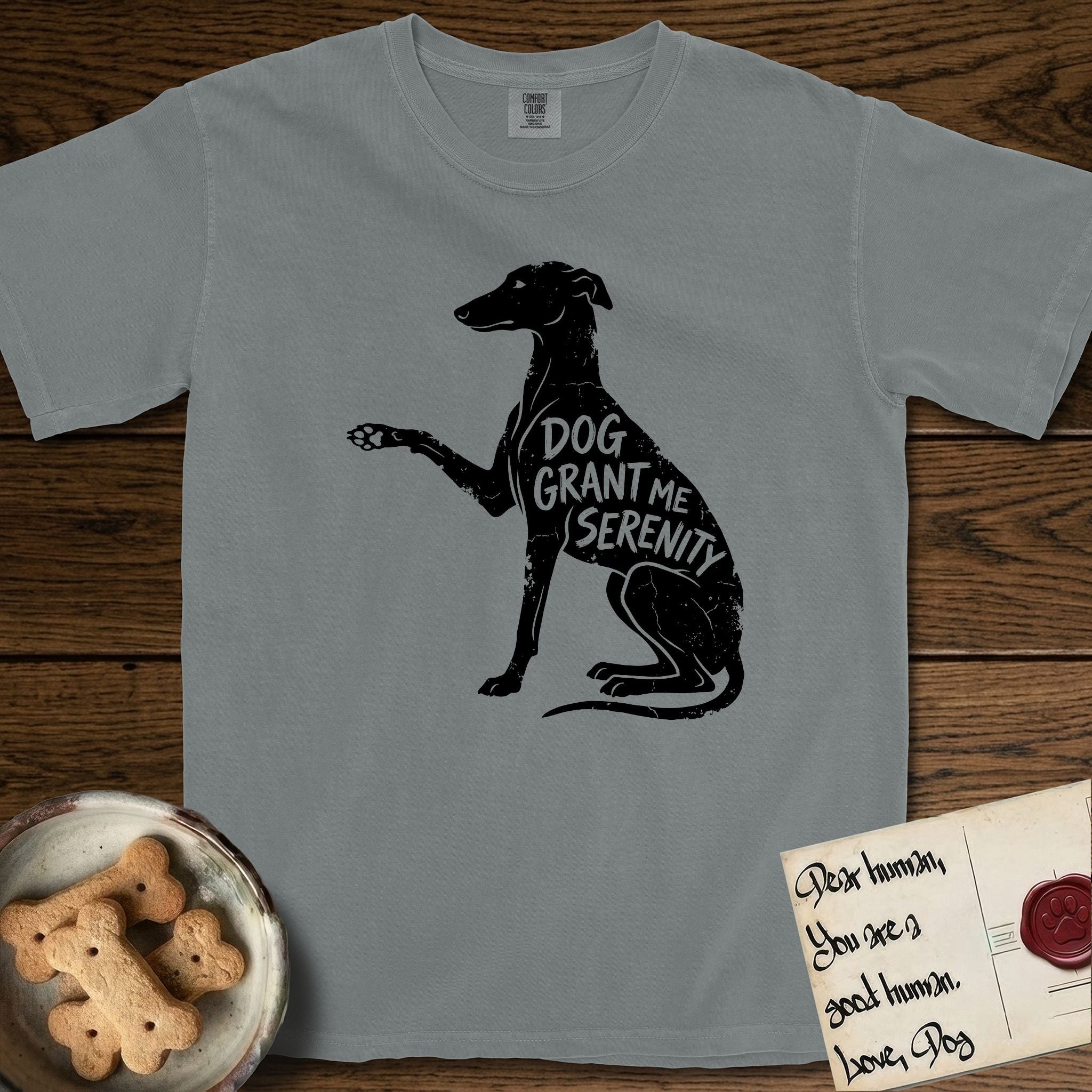 Serenity Greyhound T-Shirt flat lay in Granite, featuring Distressed black screen print silhouette of a Greyhound sitting in profile with one paw raised, an arched back and a long whip tail, the words DOG GRANT ME SERENITY showing through her body in the shirt color.