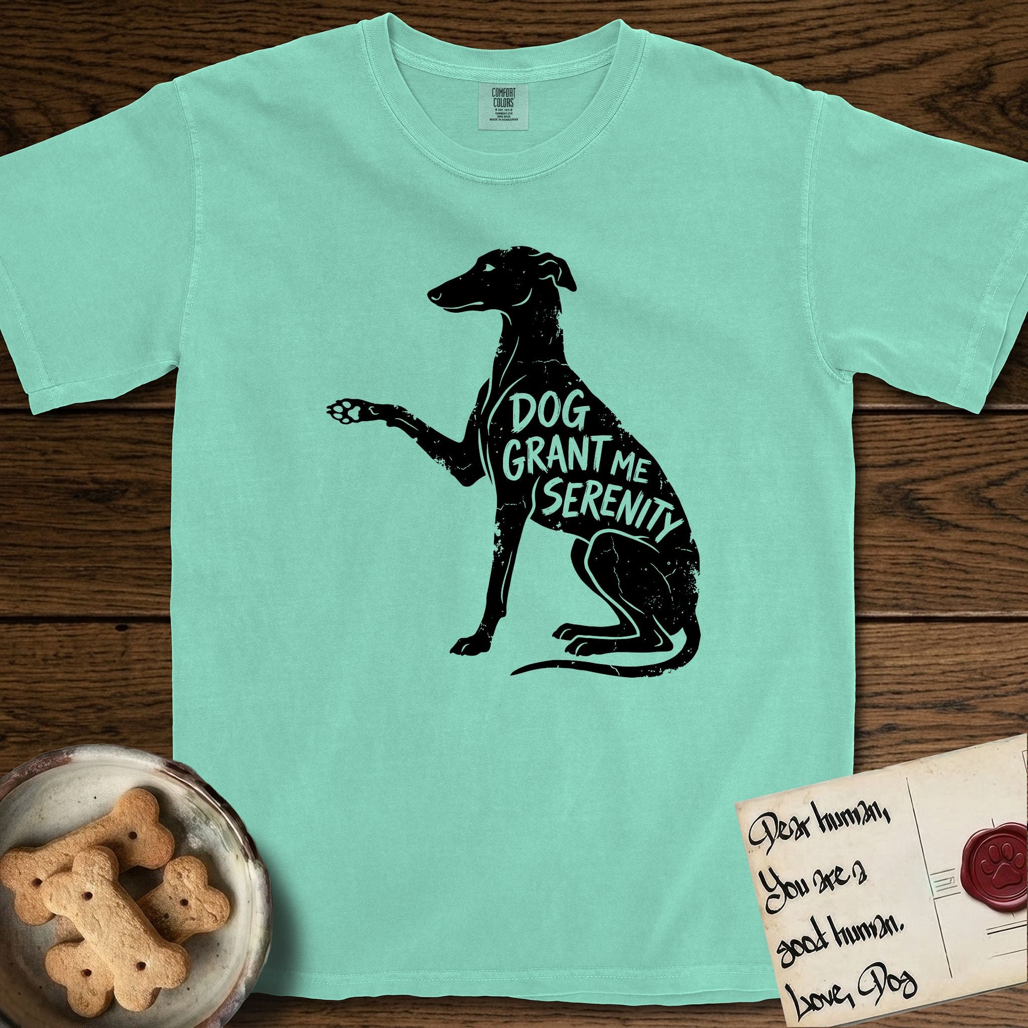 Serenity Greyhound T-Shirt flat lay in Island Reef, featuring Distressed black screen print silhouette of a Greyhound sitting in profile with one paw raised, an arched back and a long whip tail, the words DOG GRANT ME SERENITY showing through her body in the shirt color.