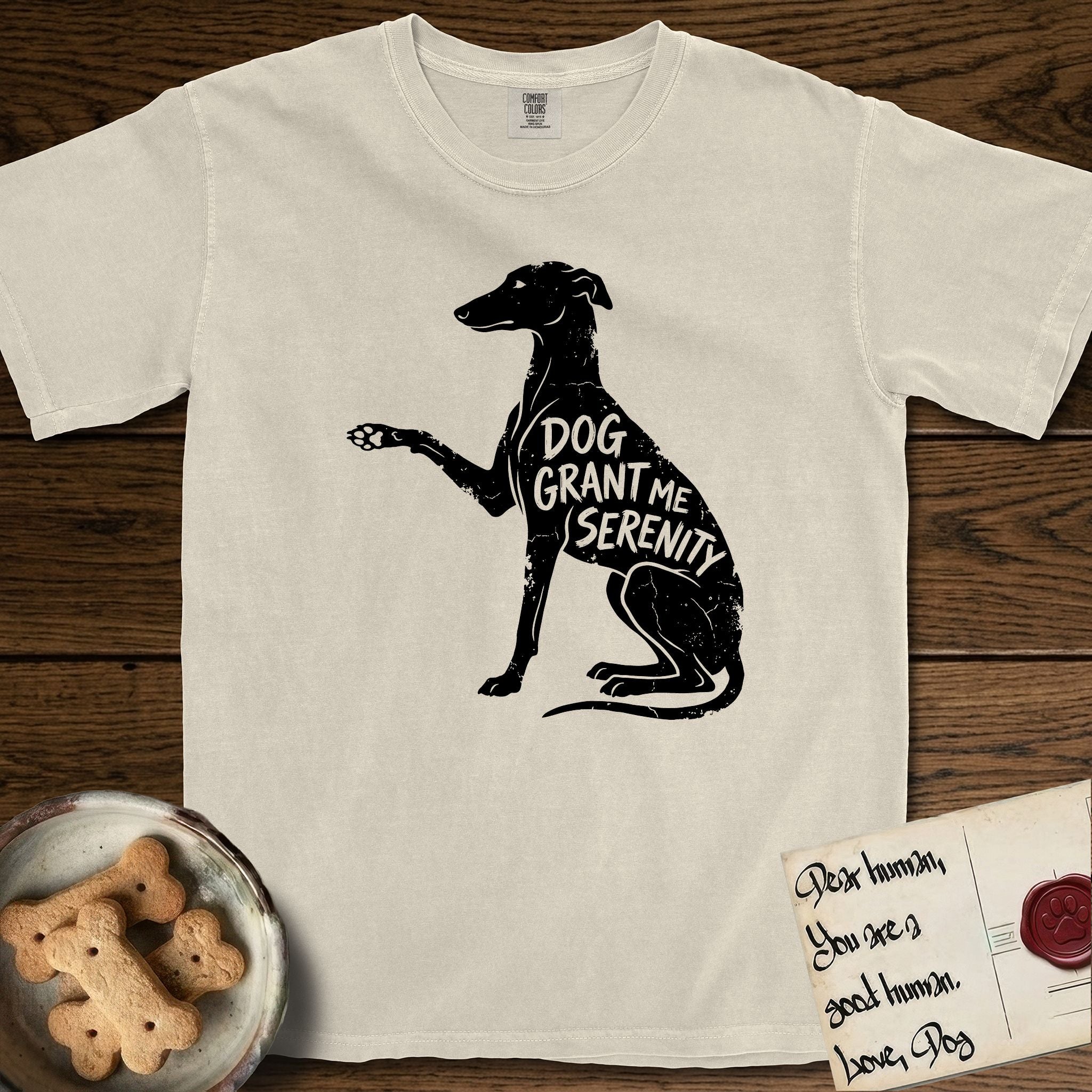 Serenity Greyhound T-Shirt flat lay in Ivory, featuring Distressed black screen print silhouette of a Greyhound sitting in profile with one paw raised, an arched back and a long whip tail, the words DOG GRANT ME SERENITY showing through her body in the shirt color.