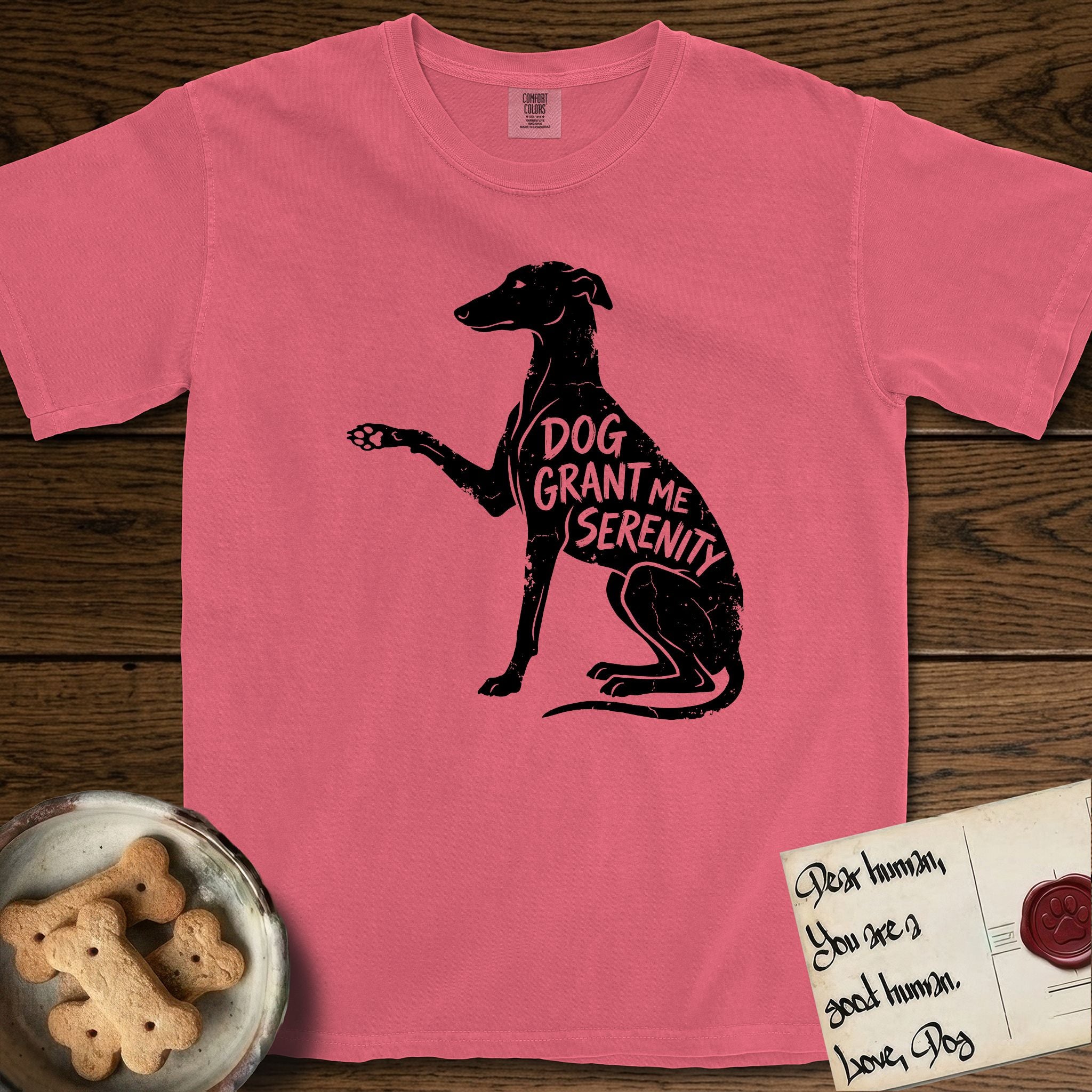 Serenity Greyhound T-Shirt flat lay in Watermelon, featuring Distressed black screen print silhouette of a Greyhound sitting in profile with one paw raised, an arched back and a long whip tail, the words DOG GRANT ME SERENITY showing through her body in the shirt color.