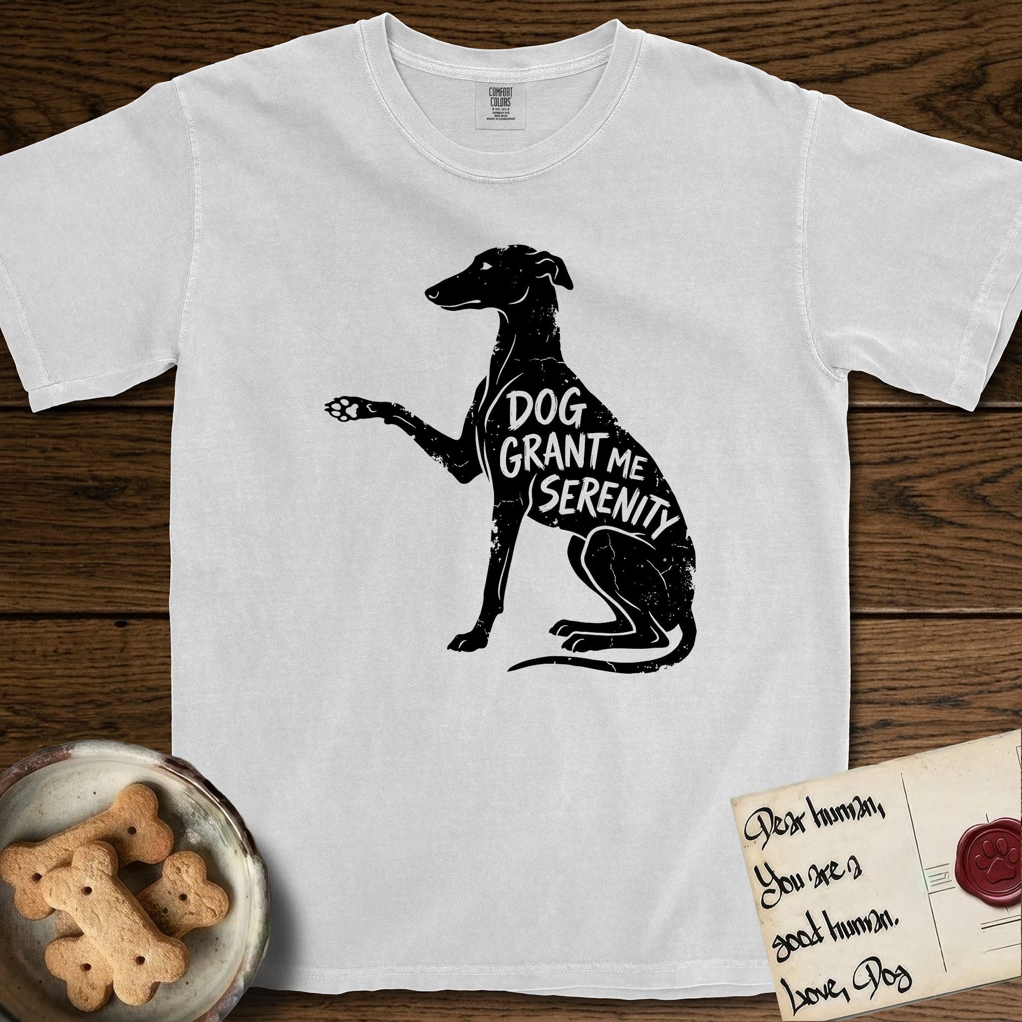 Serenity Greyhound T-Shirt flat lay in White, featuring Distressed black screen print silhouette of a Greyhound sitting in profile with one paw raised, an arched back and a long whip tail, the words DOG GRANT ME SERENITY showing through her body in the shirt color.