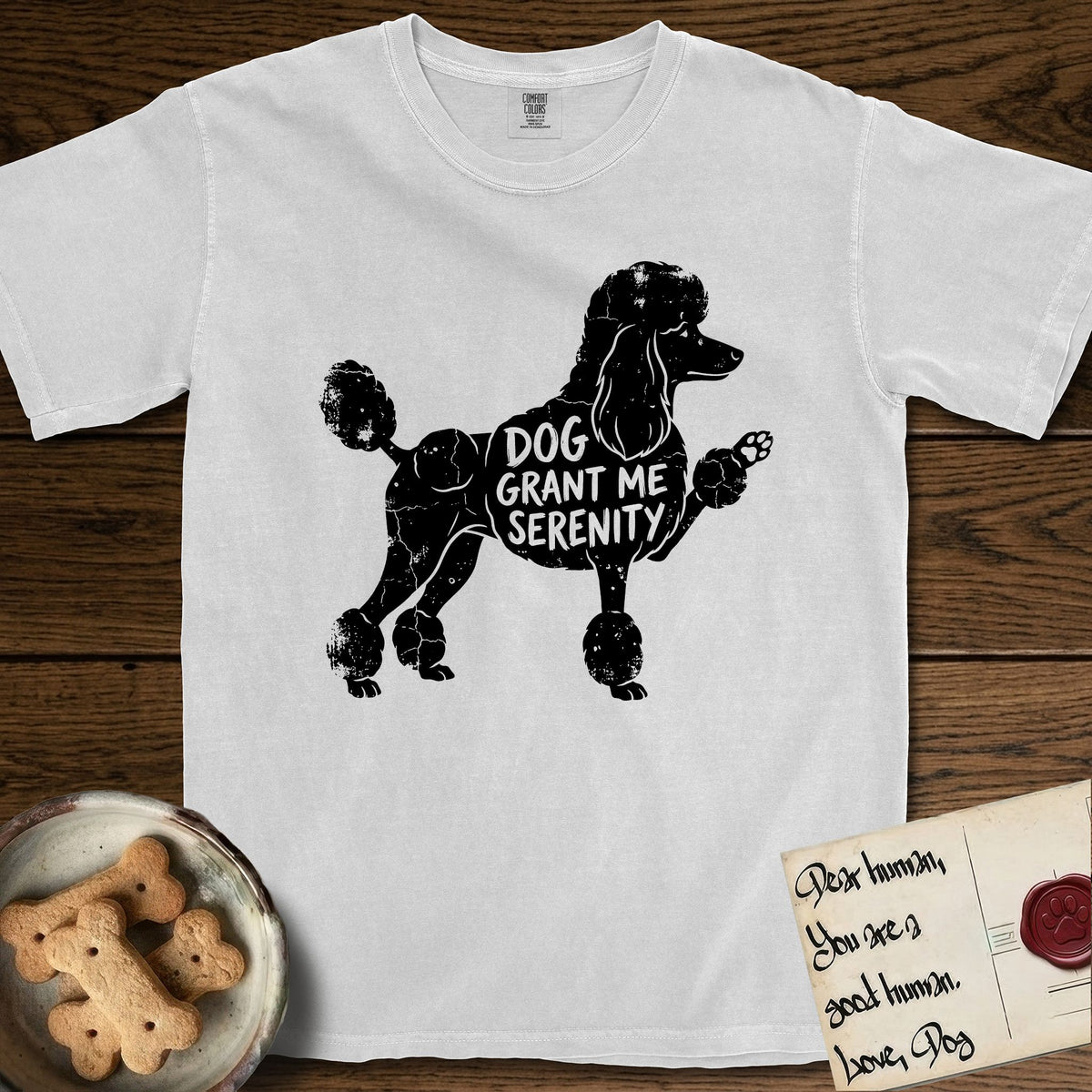 Serenity Poodle T-Shirt flat lay in White, featuring Distressed black screen print silhouette of a Poodle standing in profile with one paw raised, in a continental clip with a topknot and pompons, the words DOG GRANT ME SERENITY showing through her body in the shirt color.