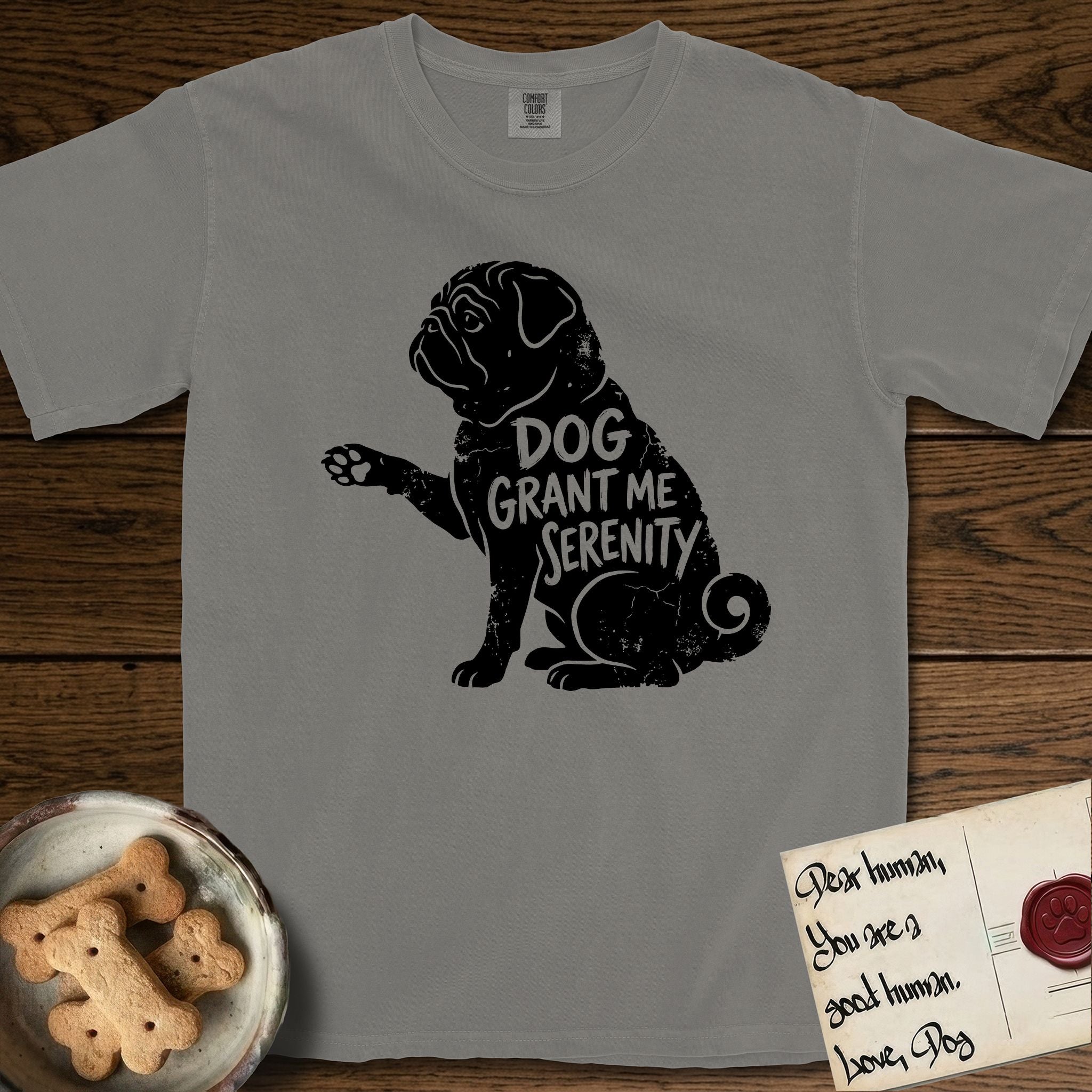 Serenity Pug T-Shirt flat lay in Grey, featuring Distressed black screen print silhouette of a Pug sitting in profile with one paw raised, a wrinkled face and a tightly curled tail, the words DOG GRANT ME SERENITY showing through his body in the shirt color.