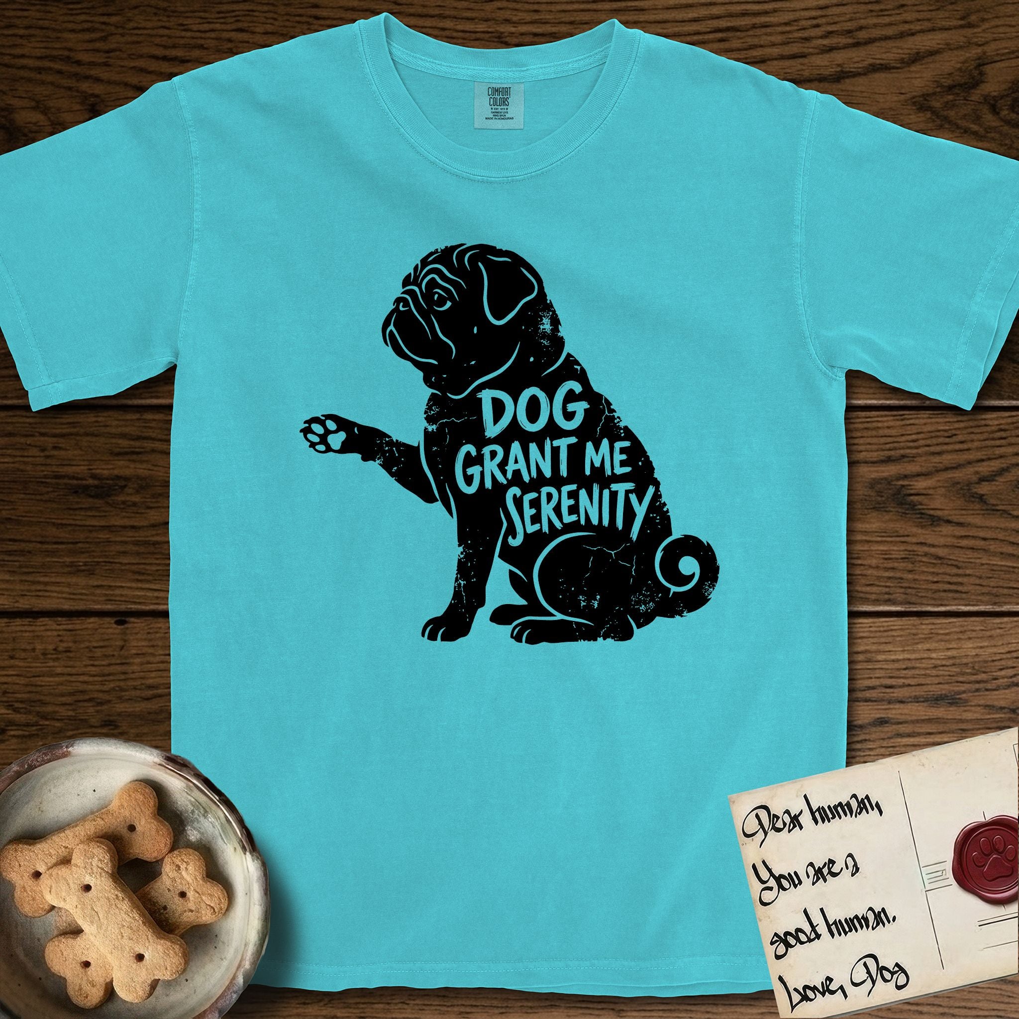 Serenity Pug T-Shirt flat lay in Lagoon Blue, featuring Distressed black screen print silhouette of a Pug sitting in profile with one paw raised, a wrinkled face and a tightly curled tail, the words DOG GRANT ME SERENITY showing through his body in the shirt color.