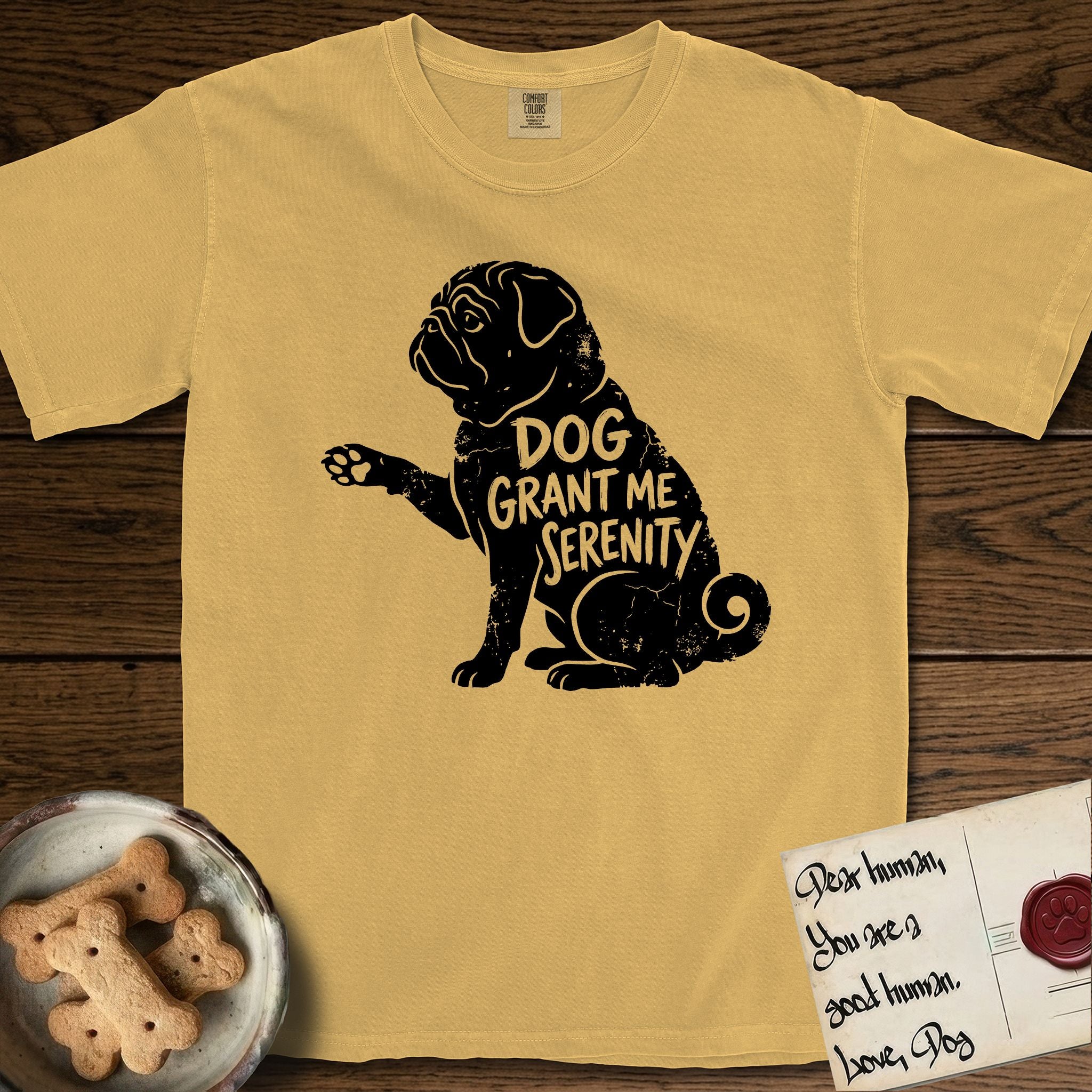 Serenity Pug T-Shirt flat lay in Mustard, featuring Distressed black screen print silhouette of a Pug sitting in profile with one paw raised, a wrinkled face and a tightly curled tail, the words DOG GRANT ME SERENITY showing through his body in the shirt color.