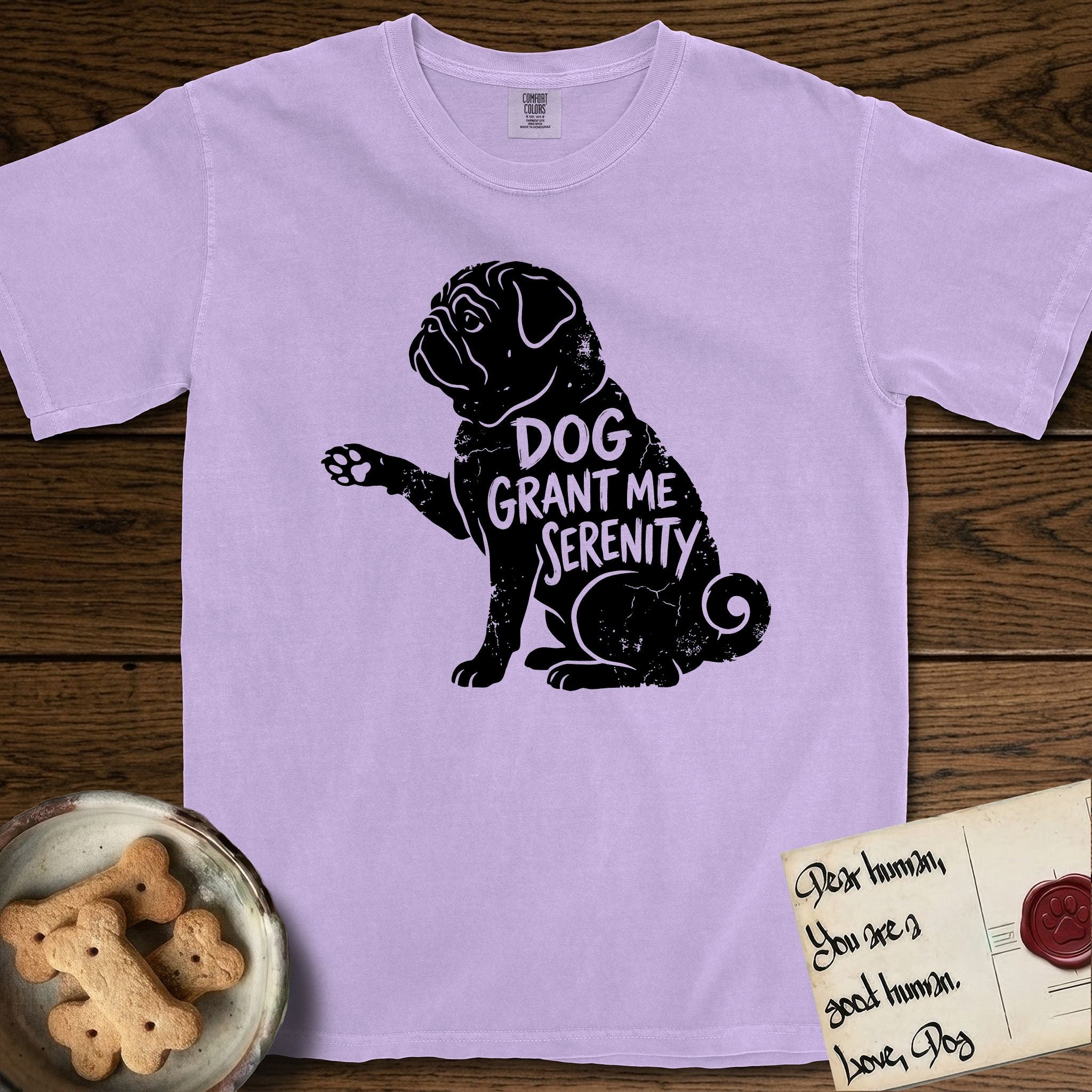 Serenity Pug T-Shirt flat lay in Orchid, featuring Distressed black screen print silhouette of a Pug sitting in profile with one paw raised, a wrinkled face and a tightly curled tail, the words DOG GRANT ME SERENITY showing through his body in the shirt color.