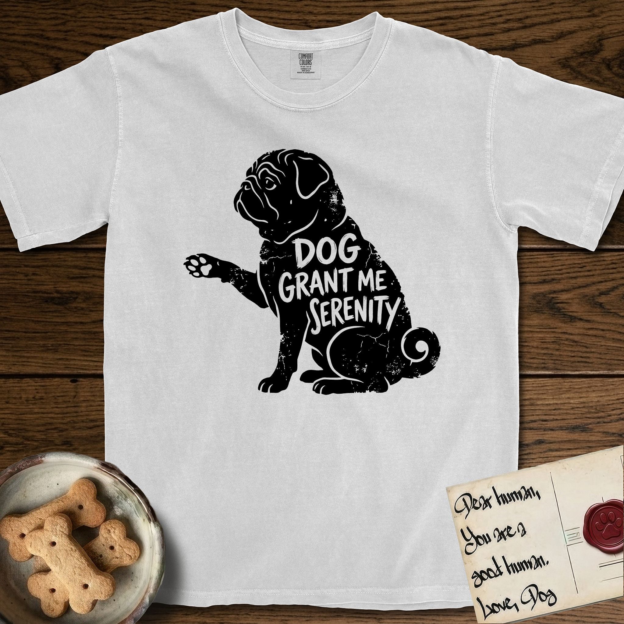 Serenity Pug T-Shirt flat lay in White, featuring Distressed black screen print silhouette of a Pug sitting in profile with one paw raised, a wrinkled face and a tightly curled tail, the words DOG GRANT ME SERENITY showing through his body in the shirt color.