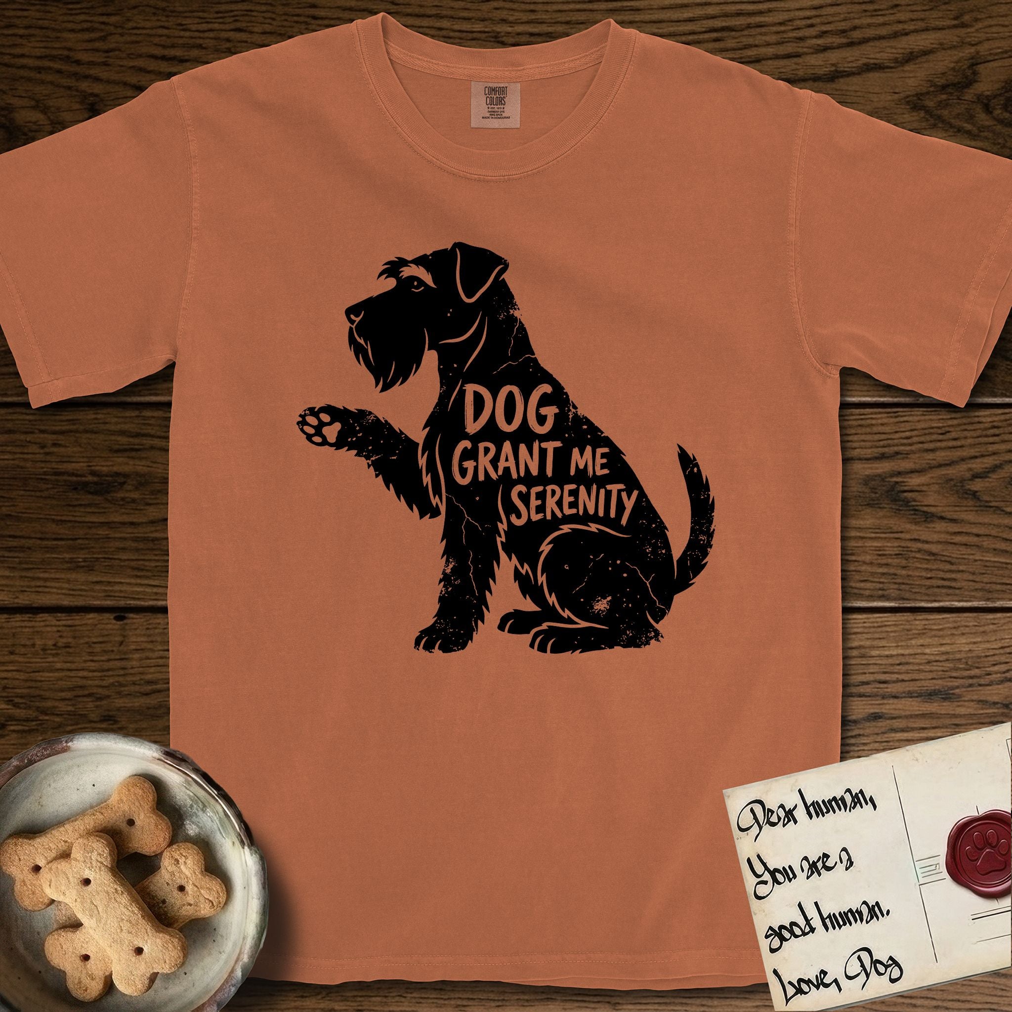 Serenity Schnauzer T-Shirt flat lay in Yam, featuring Distressed black screen print silhouette of a Schnauzer sitting in profile with one paw raised, a long beard and bushy eyebrows, the words DOG GRANT ME SERENITY showing through her body in the shirt color.