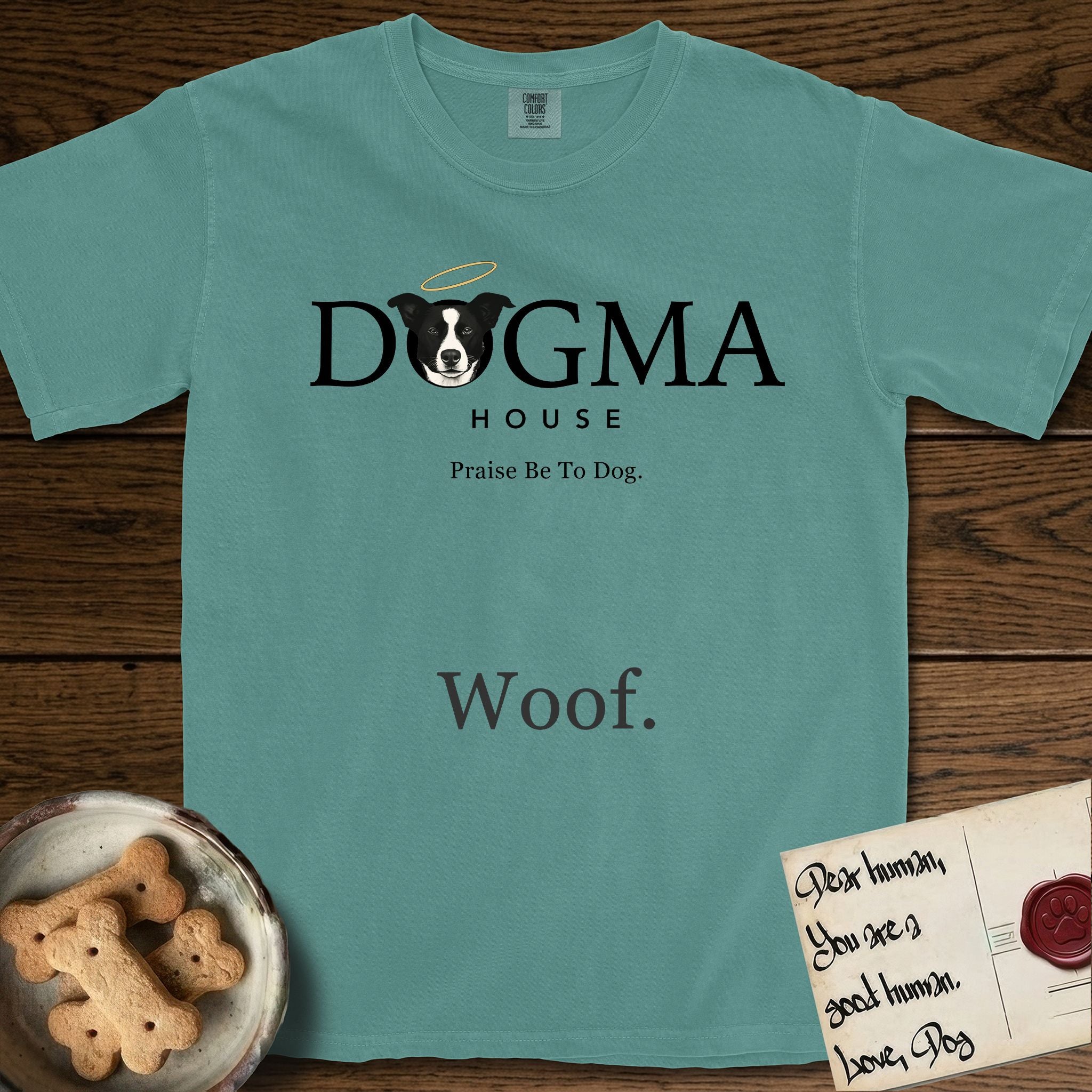 Dogma House Dark Logo T-Shirt flat lay in Blue Spruce, featuring the Dogma House wordmark in dark ink with Lobo the mascot forming the O, a halo above him, and HOUSE below.