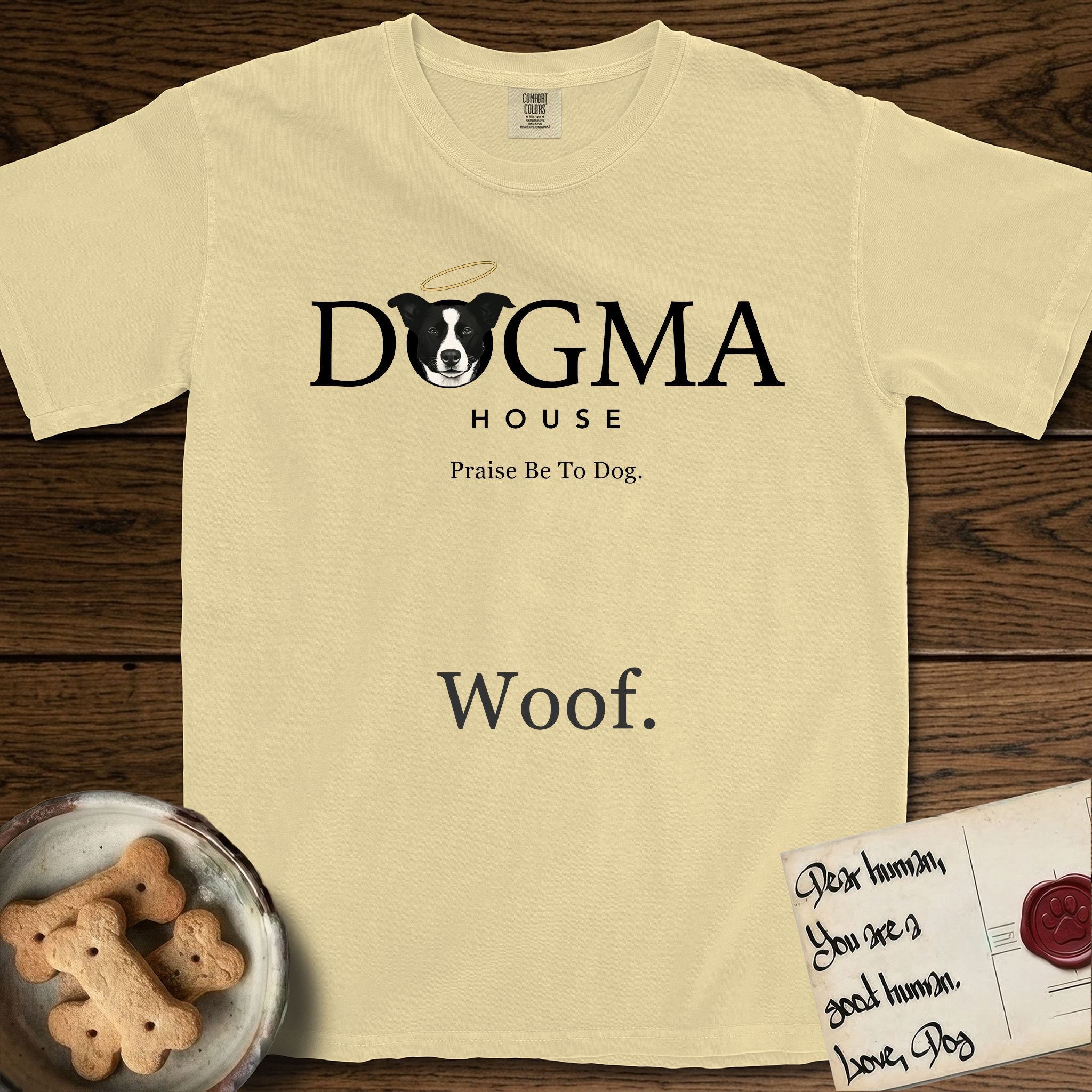 Dogma House Dark Logo T-Shirt flat lay in Butter, featuring the Dogma House wordmark in dark ink with Lobo the mascot forming the O, a halo above him, and HOUSE below.