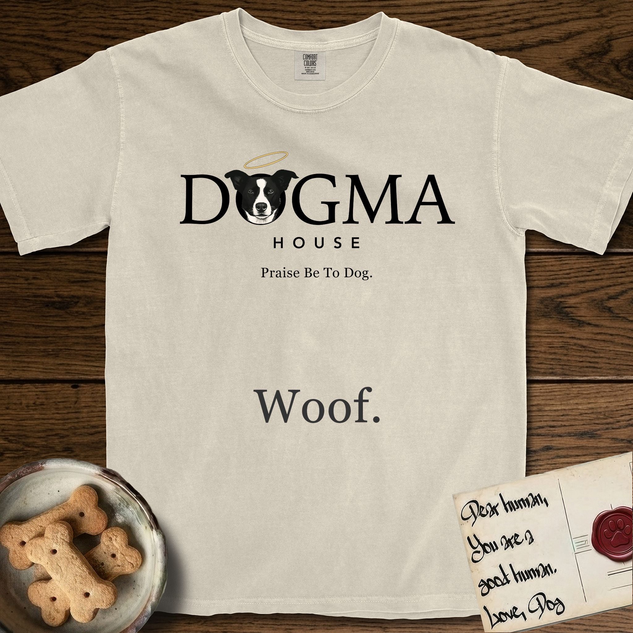 Dogma House Dark Logo T-Shirt flat lay in Ivory, featuring the Dogma House wordmark in dark ink with Lobo the mascot forming the O, a halo above him, and HOUSE below.