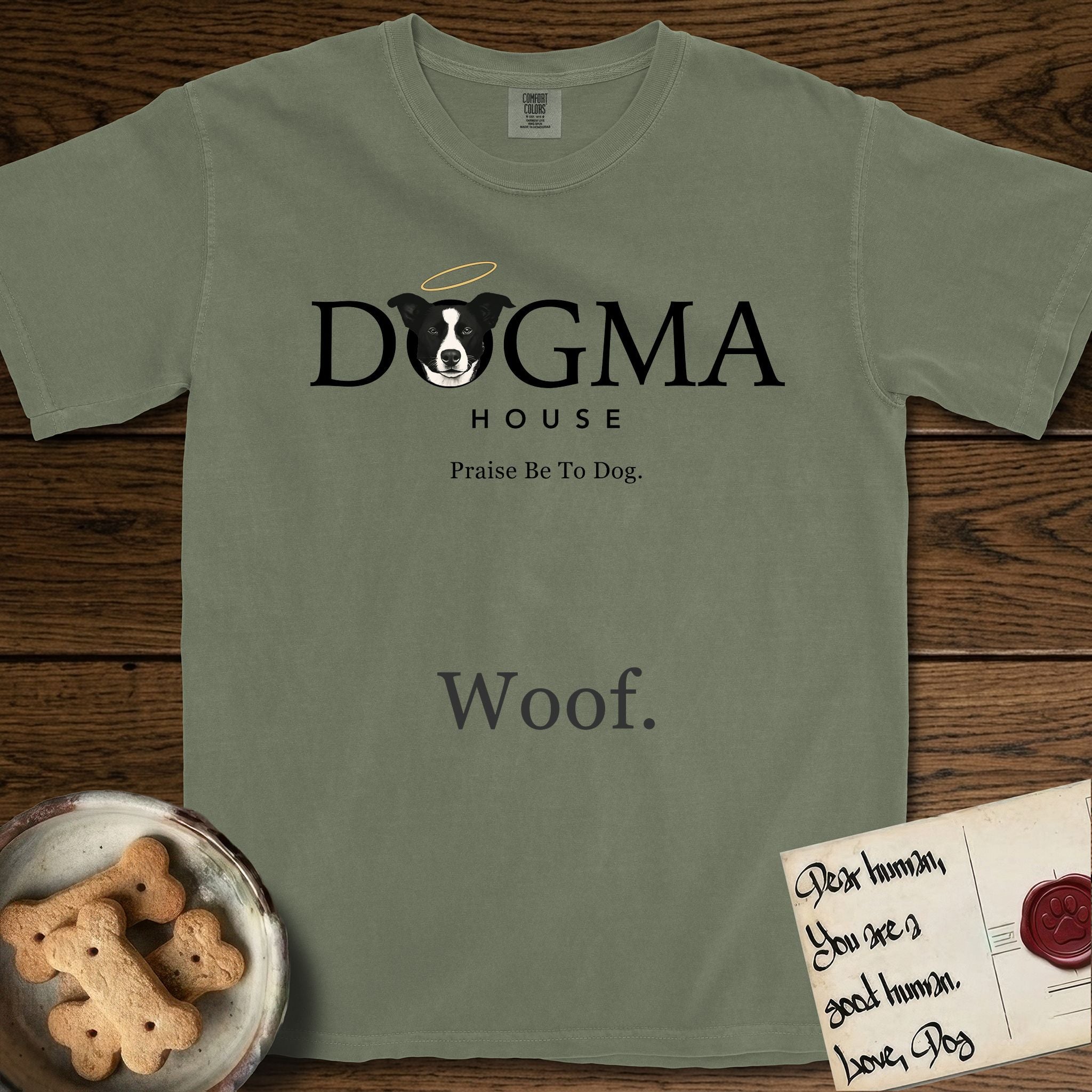 Dogma House Dark Logo T-Shirt flat lay in Sage, featuring the Dogma House wordmark in dark ink with Lobo the mascot forming the O, a halo above him, and HOUSE below.