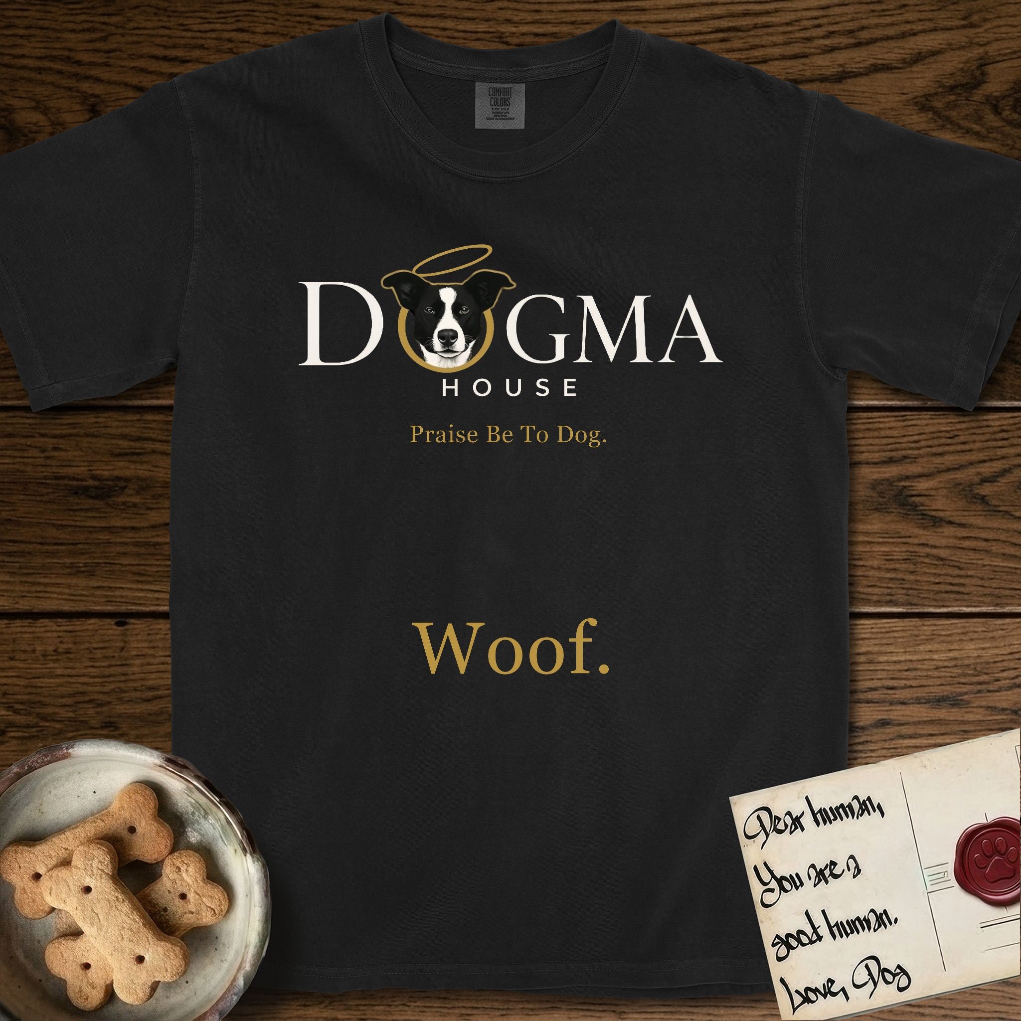 Dogma House Light Logo T-Shirt flat lay in Black, featuring the Dogma House wordmark in light ink with Lobo the mascot forming the O, a gold halo above him, and Woof below.
