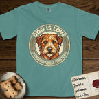 Dog is Love T-Shirt flat lay in Blue Spruce, featuring a vintage distressed circular badge with a scruffy terrier on a sage-green ground, the words Dog Is Love and Unconditional Forever, and flanking paw prints.