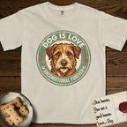 Dog is Love T-Shirt flat lay in Ivory, featuring a vintage distressed circular badge with a scruffy terrier on a sage-green ground, the words Dog Is Love and Unconditional Forever, and flanking paw prints.