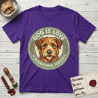 Dog is Love T-Shirt flat lay in Purple, featuring a vintage distressed circular badge with a scruffy terrier on a sage-green ground, the words Dog Is Love and Unconditional Forever, and flanking paw prints.